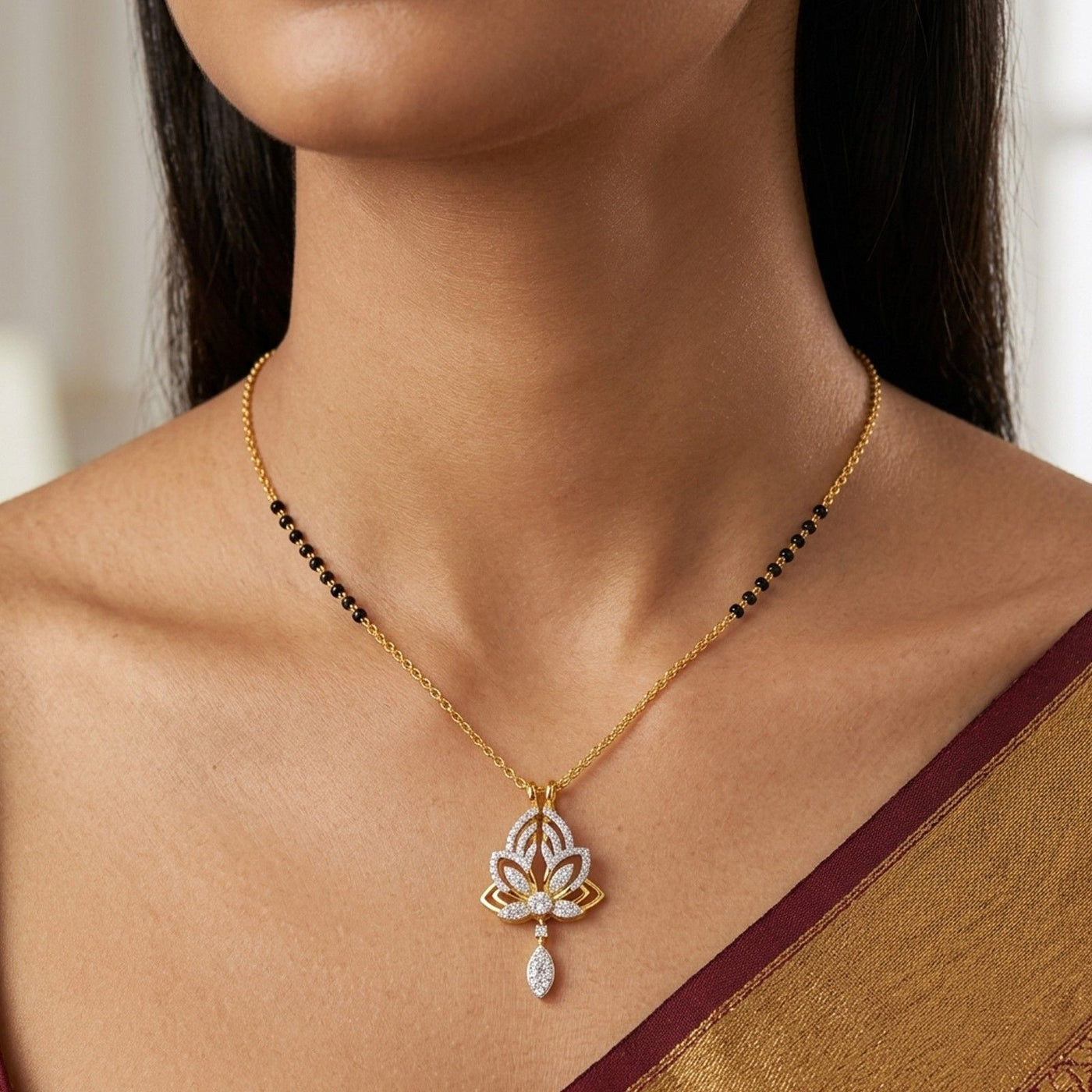 A close-up of a woman wearing a gold mangalsutra with a lotus-shaped pendant adorned with white stones and a teardrop drop