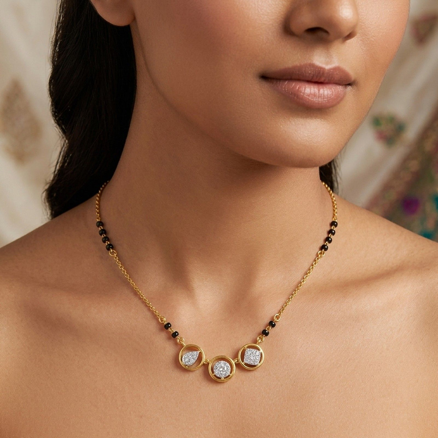 A close-up of a woman wearing a delicate gold mangalsutra with three round white stone centers and small black bead accents along the chain.