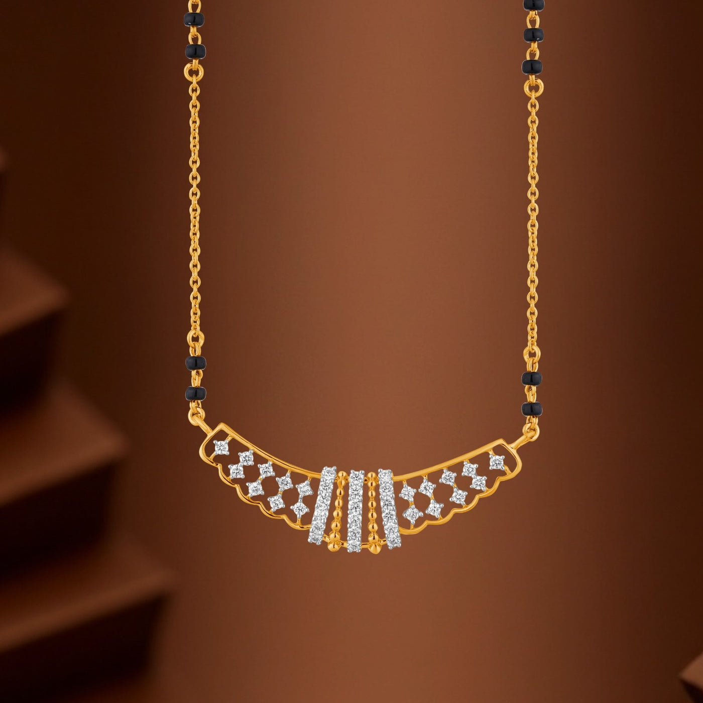 Gold necklace with a featuring black bead accents on the chain, set against a warm brown background.