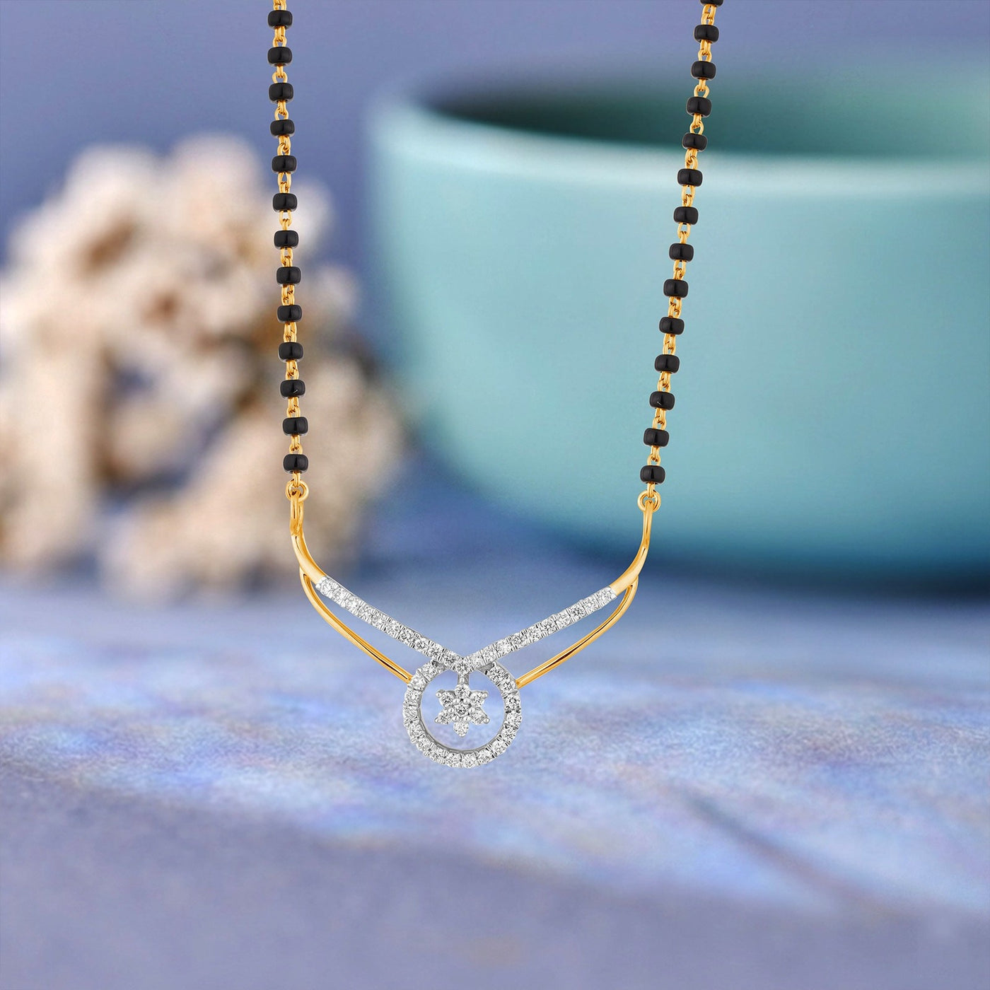 A gold-toned mangalsutra with a black beaded chain and a crescent moon adorned with clear stones, displayed against a soft blue background