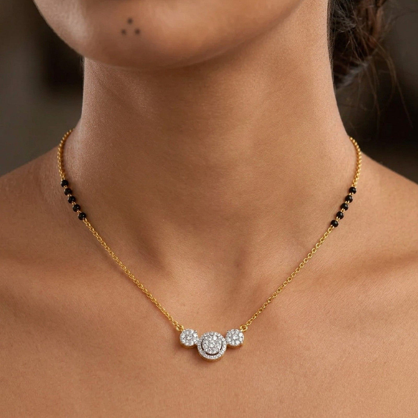 A close-up of a model's neck and collarbone wearing a delicate gold mangalsutra. 