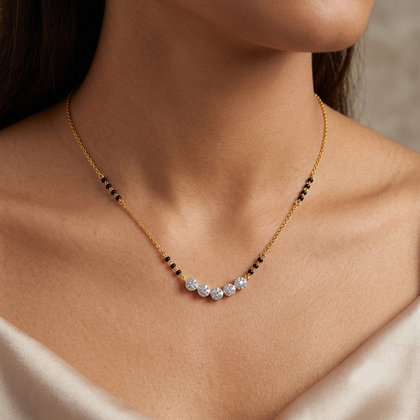 A delicate gold mangalsutra with a curved row of clear gemstones and small black bead accents, shown worn on a model's neck.