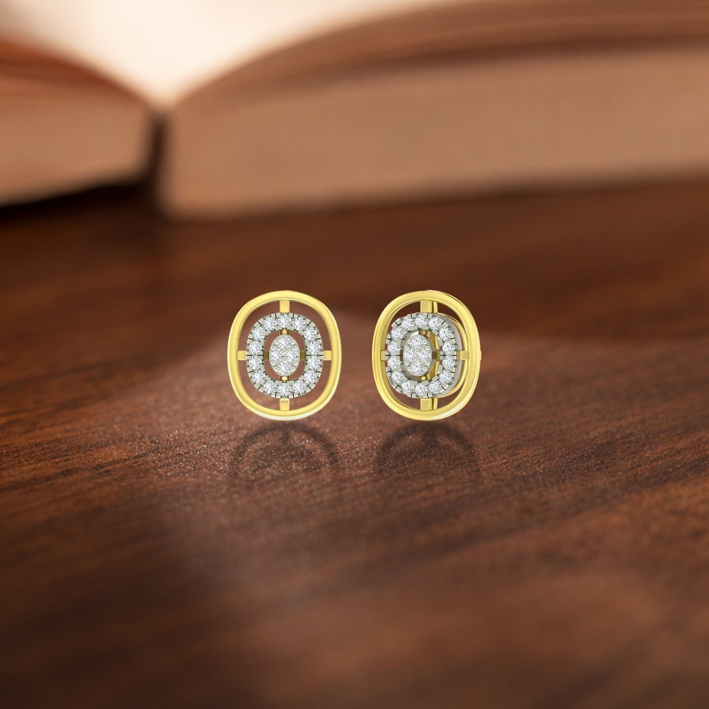 A pair of two-tone gold and diamond oval stud earrings resting on a wooden surface.