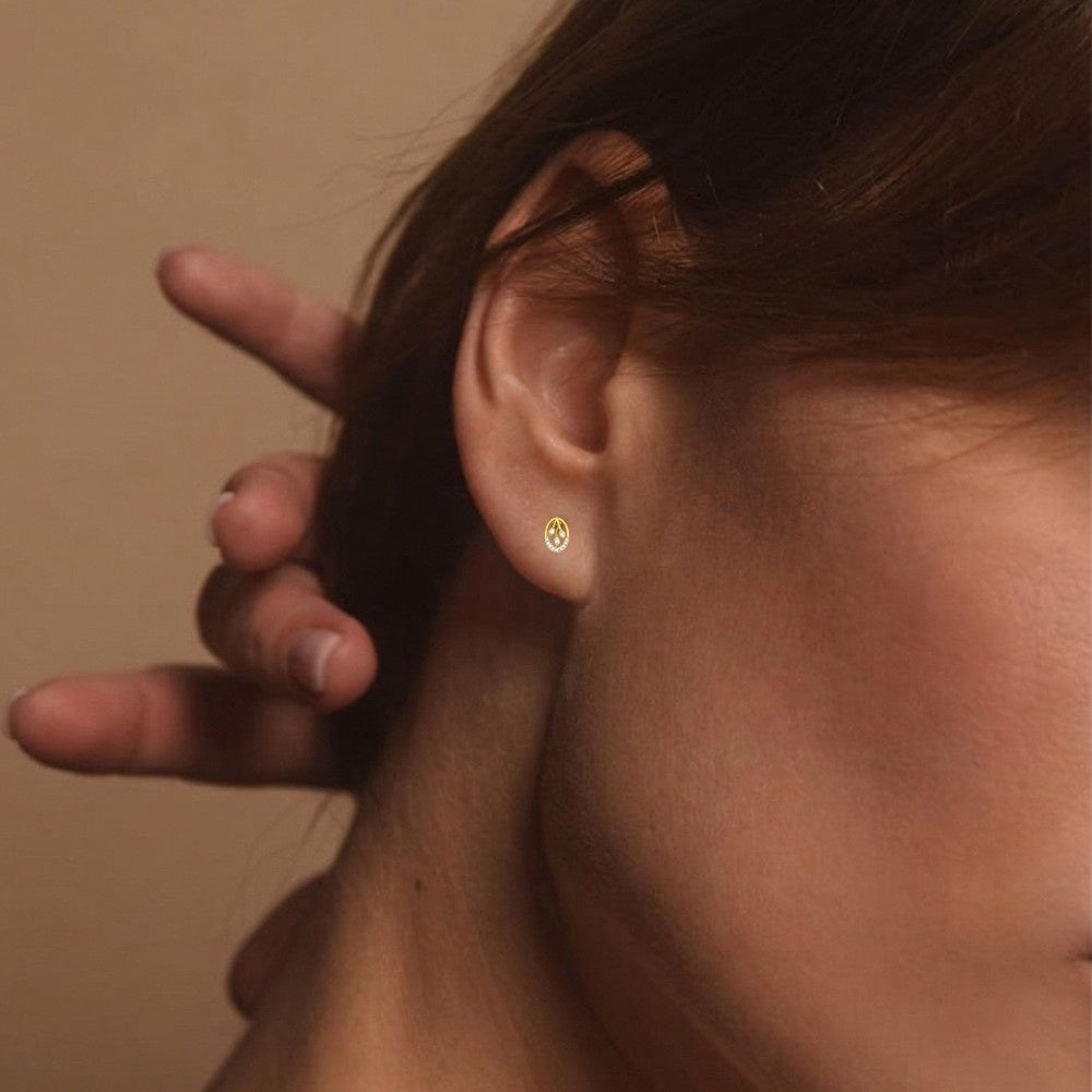 A close-up lifestyle profile shot of a woman wearing a delicate yellow gold and diamond petite oval stud earring