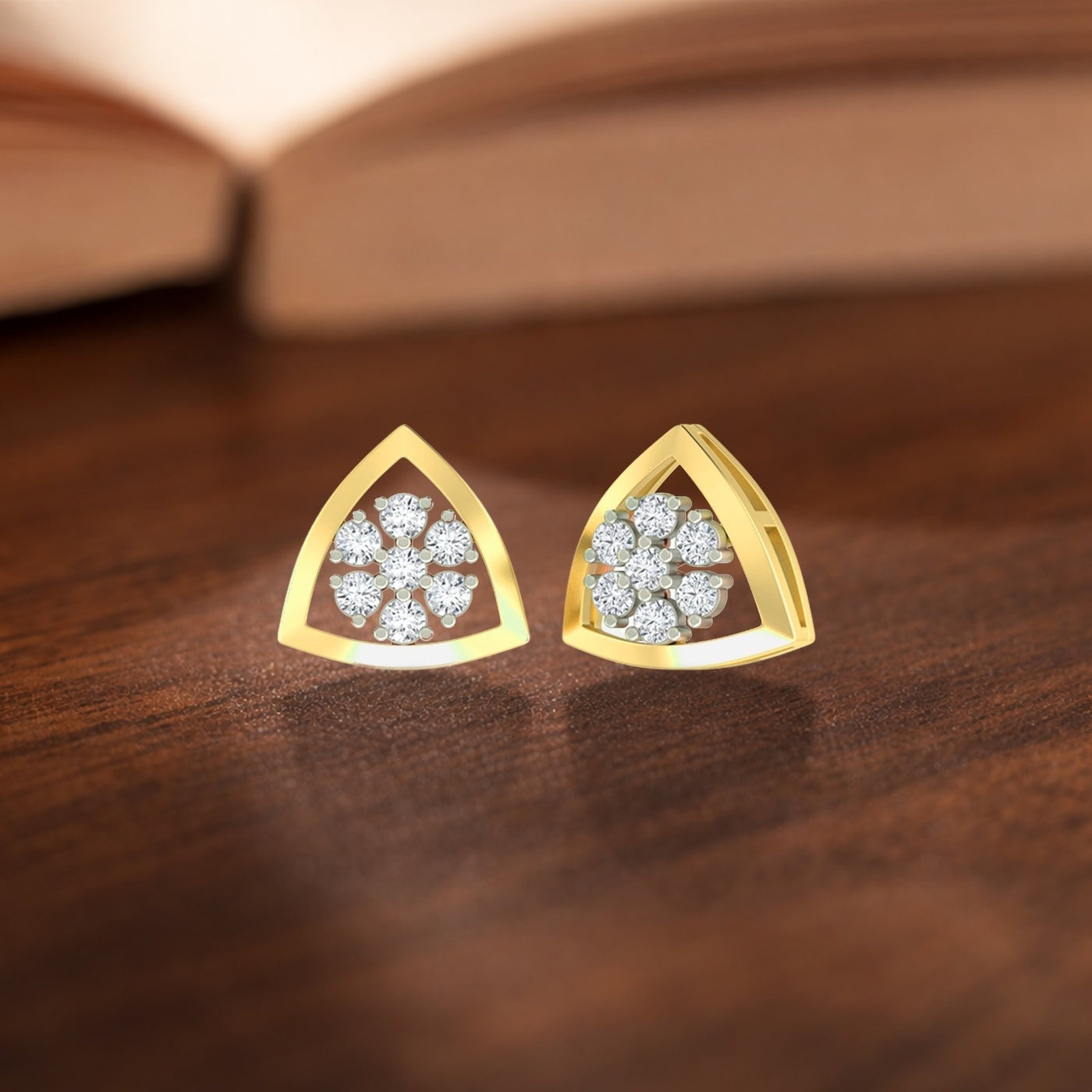 Triangular gold earrings with diamond-like stones on a wooden surface