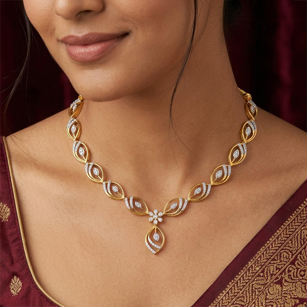 A close-up of a woman wearing a gold and diamond necklace with a teardrop, paired with a maroon embroidered saree.