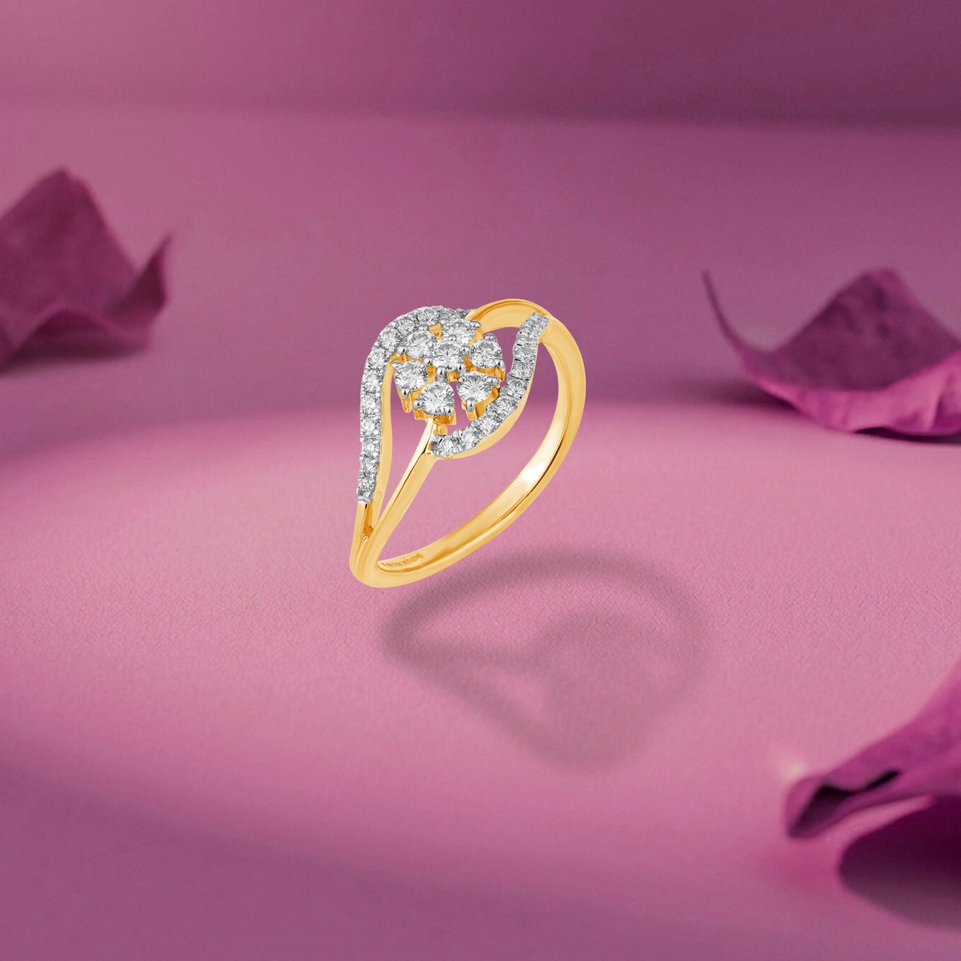 A gold ring featuring a curved, pavé-set diamond cluster, shown on a pink surface.