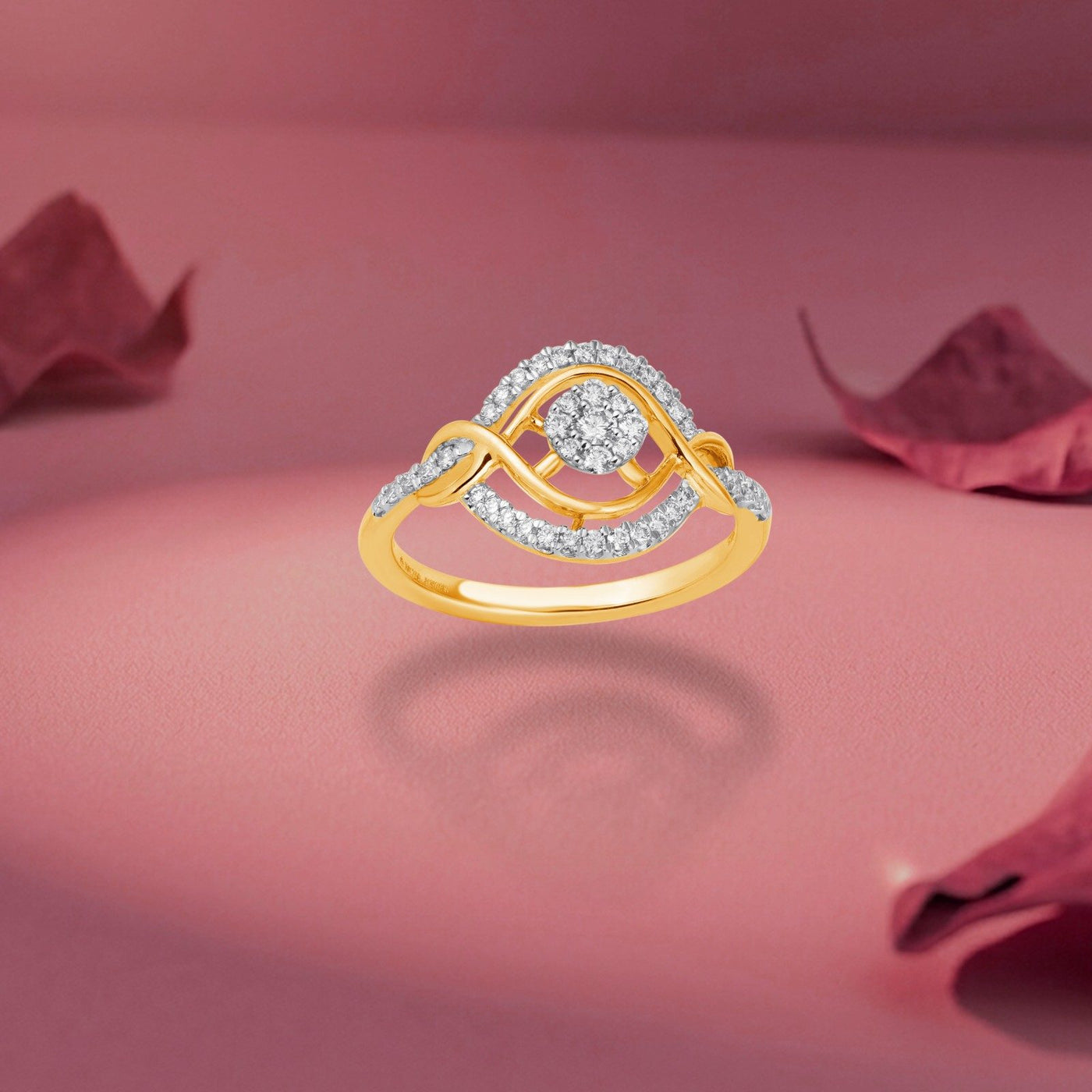 A gold ring with a circular cluster of clear stones and an eye motif, set against a soft pink background with decorative rose petals.