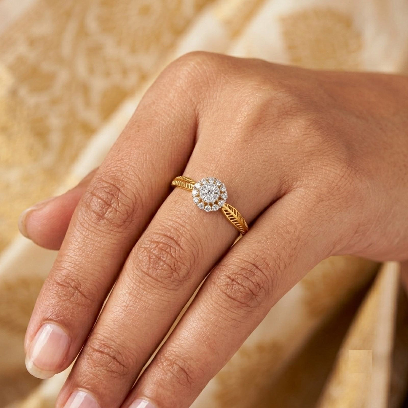 A close-up of a hand wearing a gold ring with a round diamond cluster, set against a soft beige patterned background.