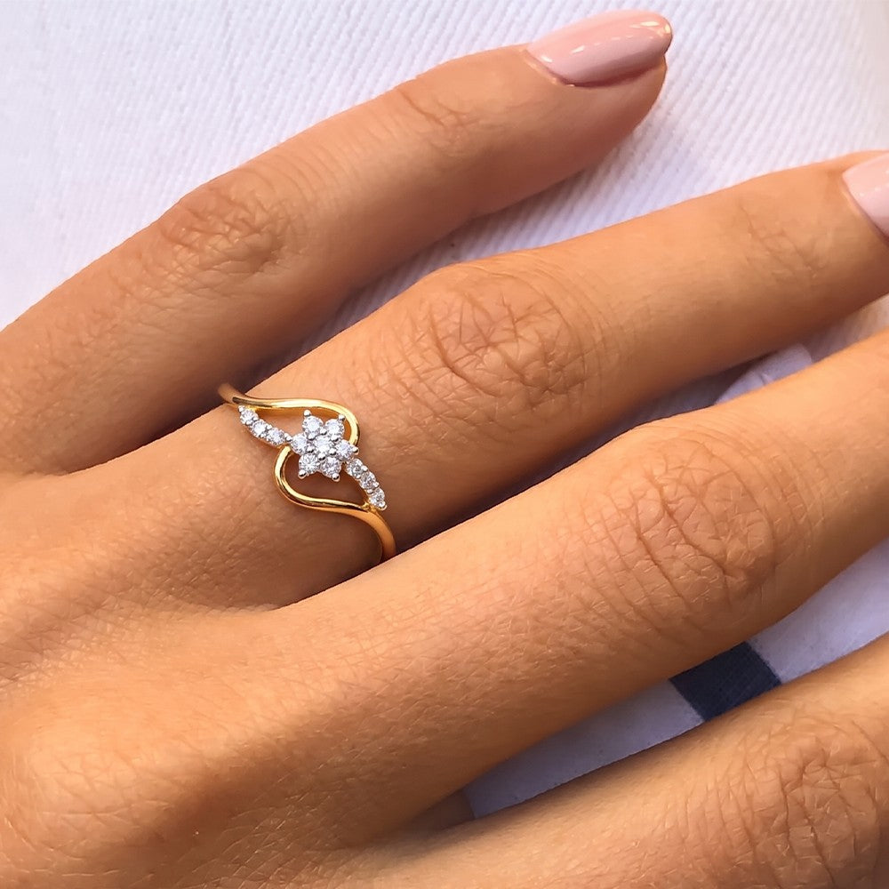 A gold and diamond ring with a floral cluster, worn on a person's ring finger against a light textured background.