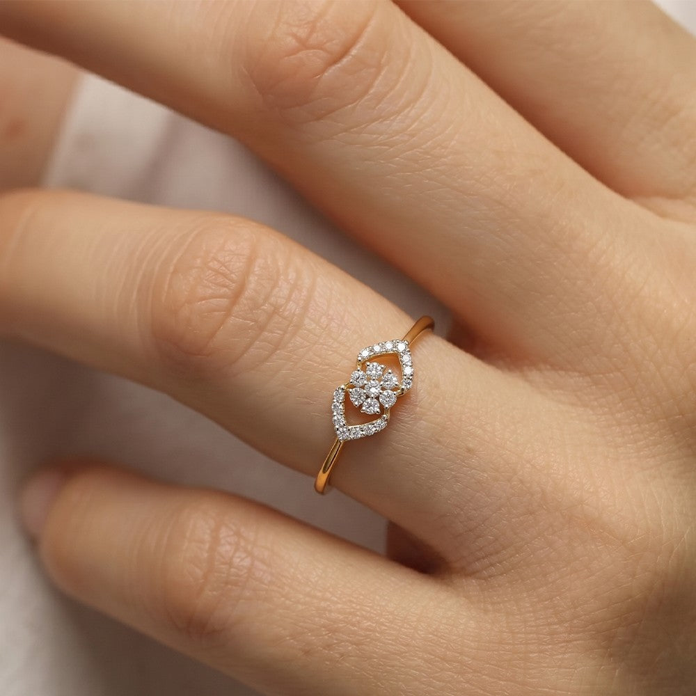 A close-up of a hand wearing a delicate gold ring with a heart-shaped cluster of small clear stones.