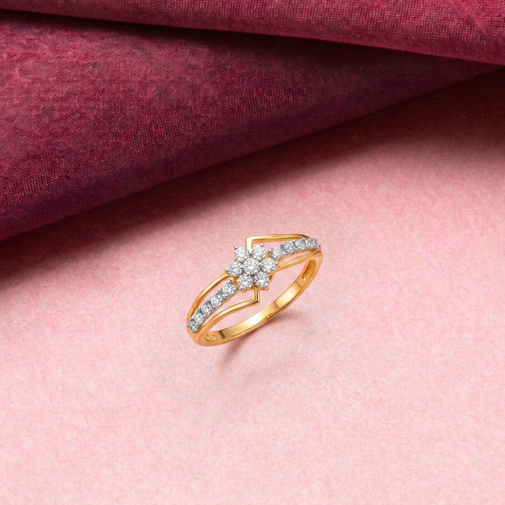 A gold ring with a diamond cluster and pavé band, displayed on a pink textured surface with a draped burgundy fabric in the background.