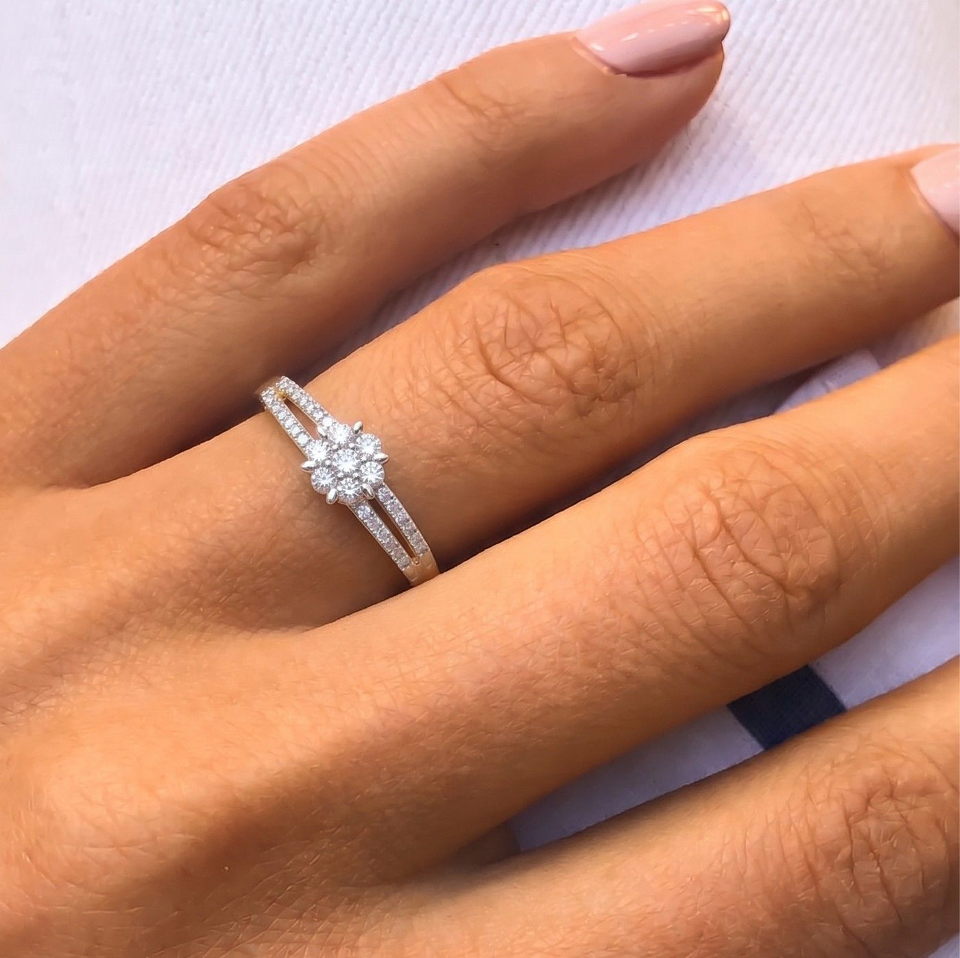 A close-up of a hand wearing with a central flower cluster of clear stones, set against a light textured background.