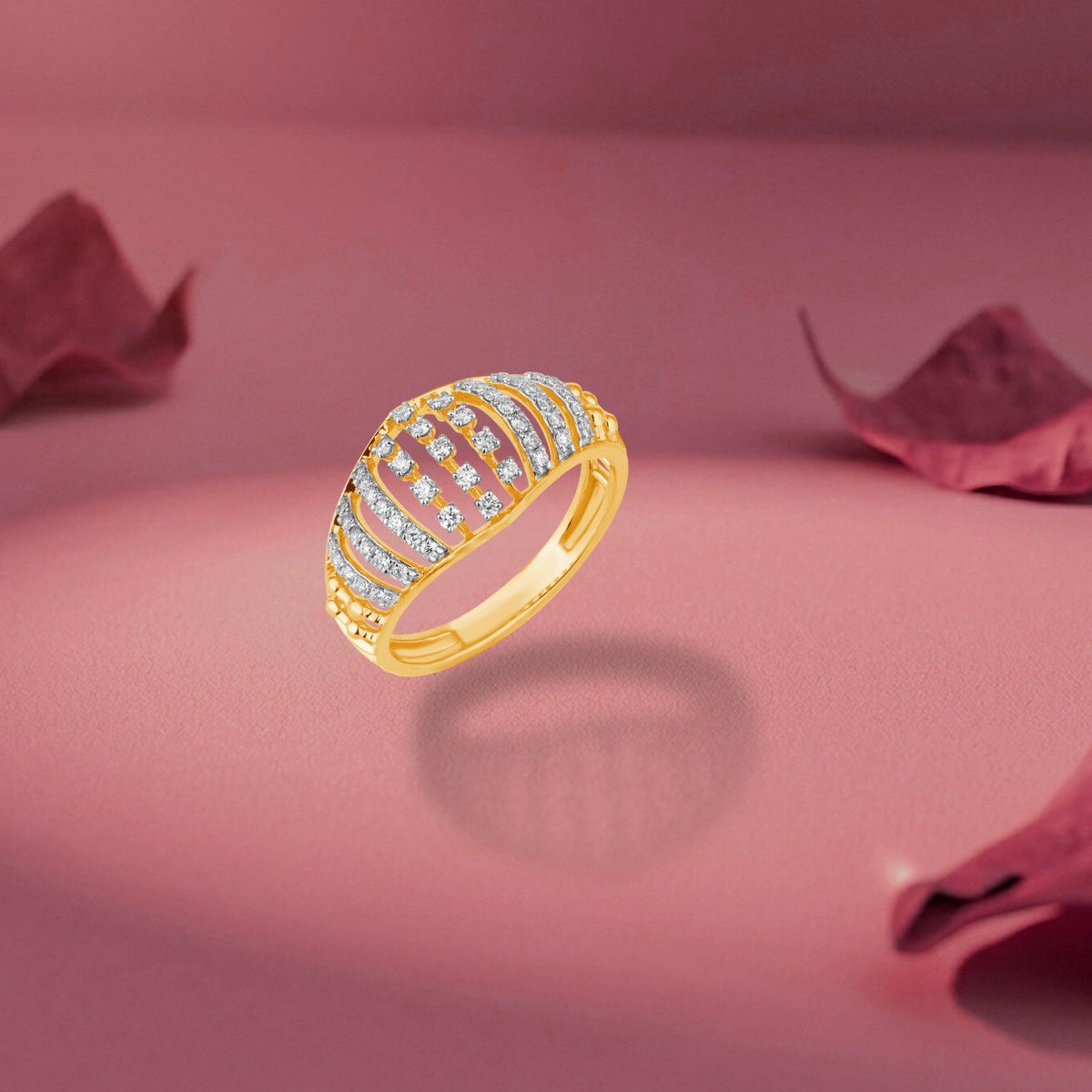 A gold and diamond ring with a curved, multi-row setting, floating on a pink reflective surface with soft rose petals in the background.