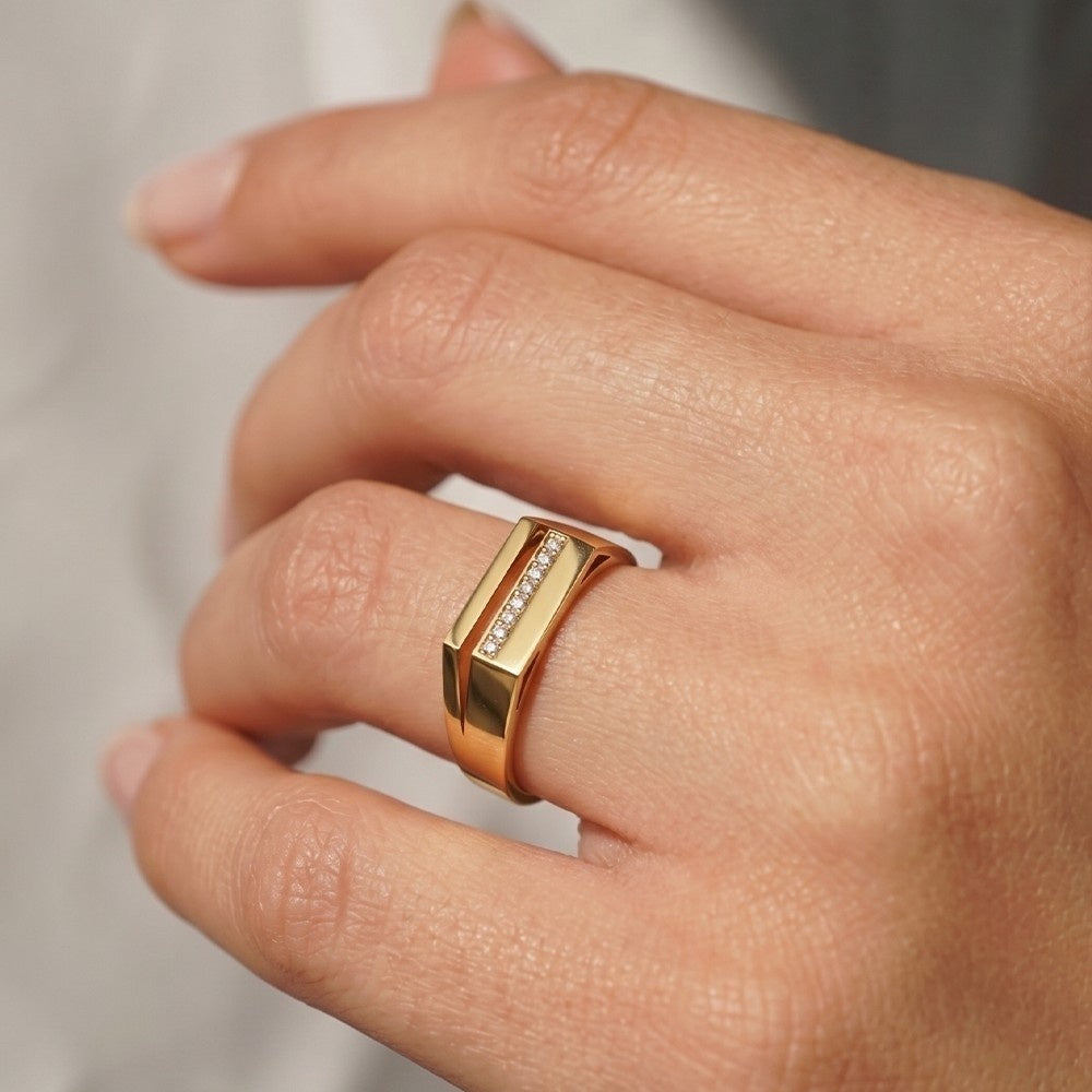 Gold ring with  diamonds on a person's finger against a neutral background.