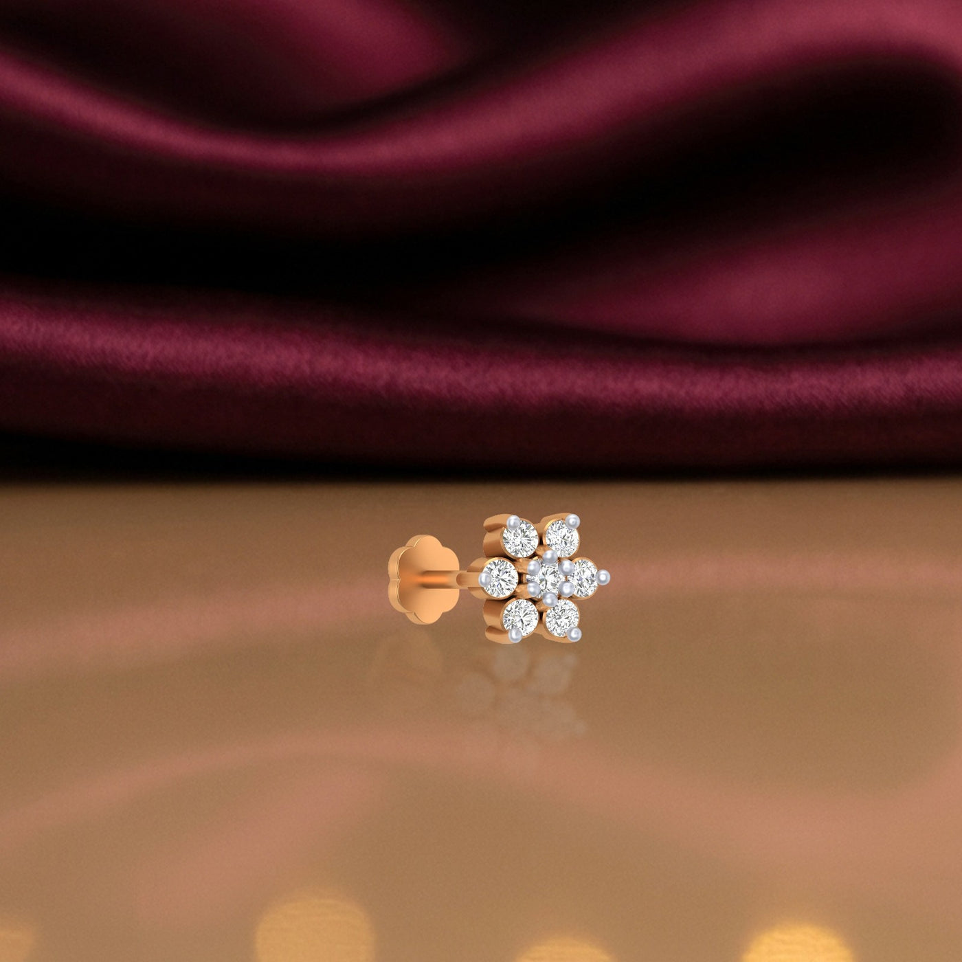 yellow gold and diamond stud nose pin with diamonds on a reflective surface and maroon fabric background