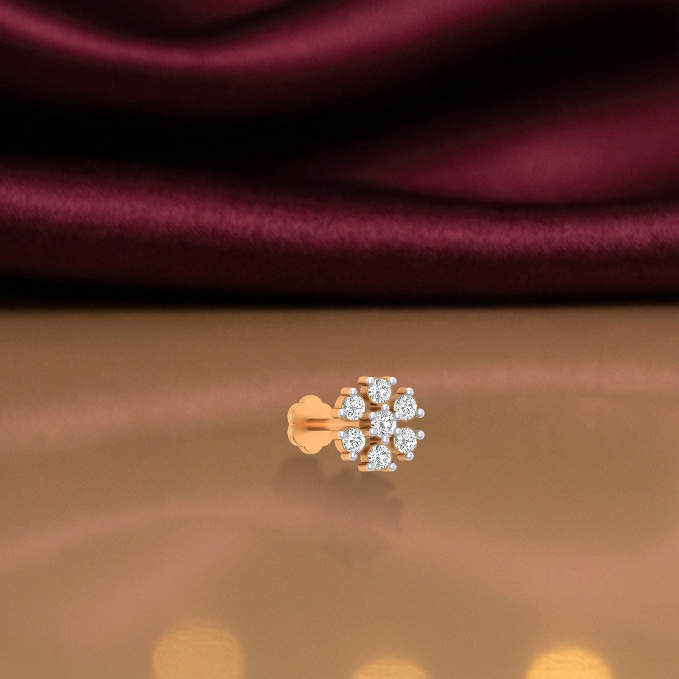 yellow gold and diamond stud nose pin on a reflective surface with a maroon fabric background