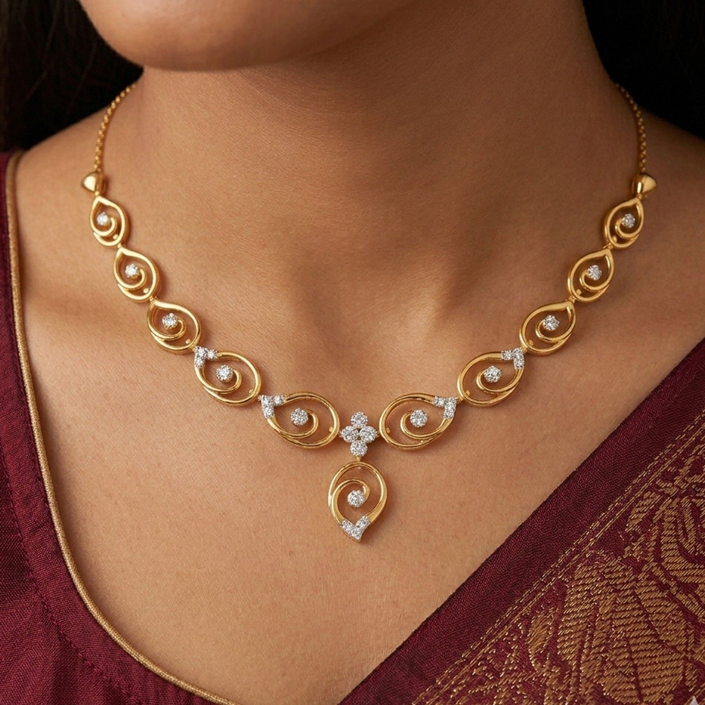 Gold and diamond necklace with diamond accents worn by a person in a maroon saree.