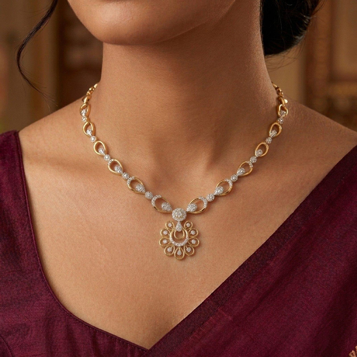 Gold necklace with a floral pendant worn by a person in a maroon outfit.