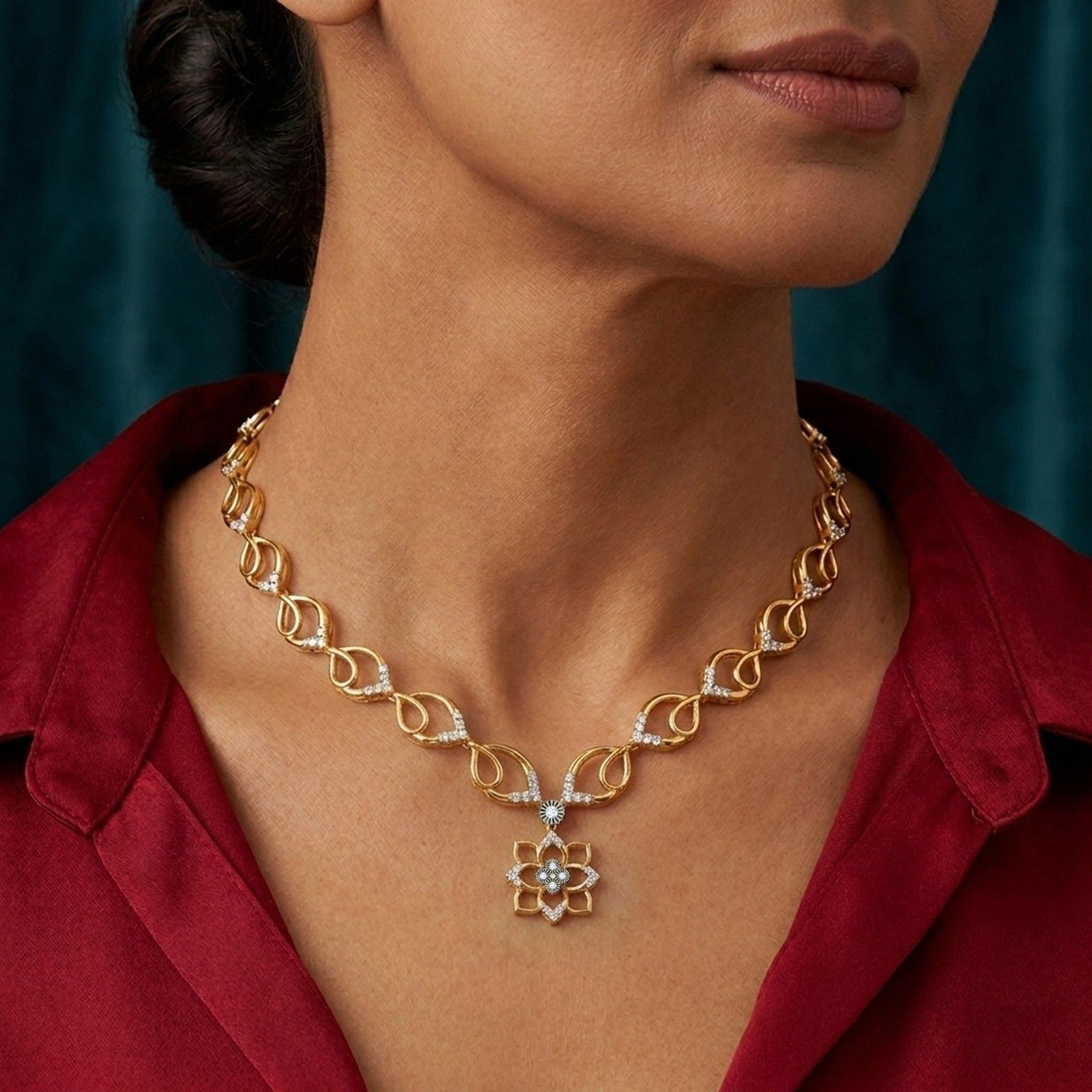 Gold necklace with floral design worn by a person in a red shirt against a teal background