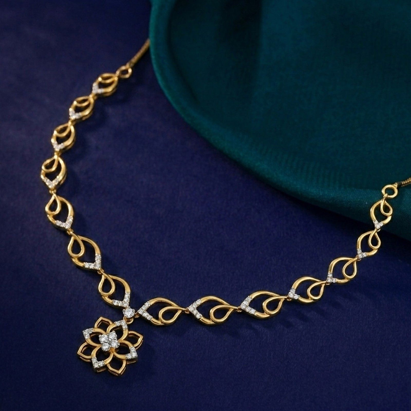 A gold and diamond necklace with a floral design, displayed on a dark navy blue fabric background.