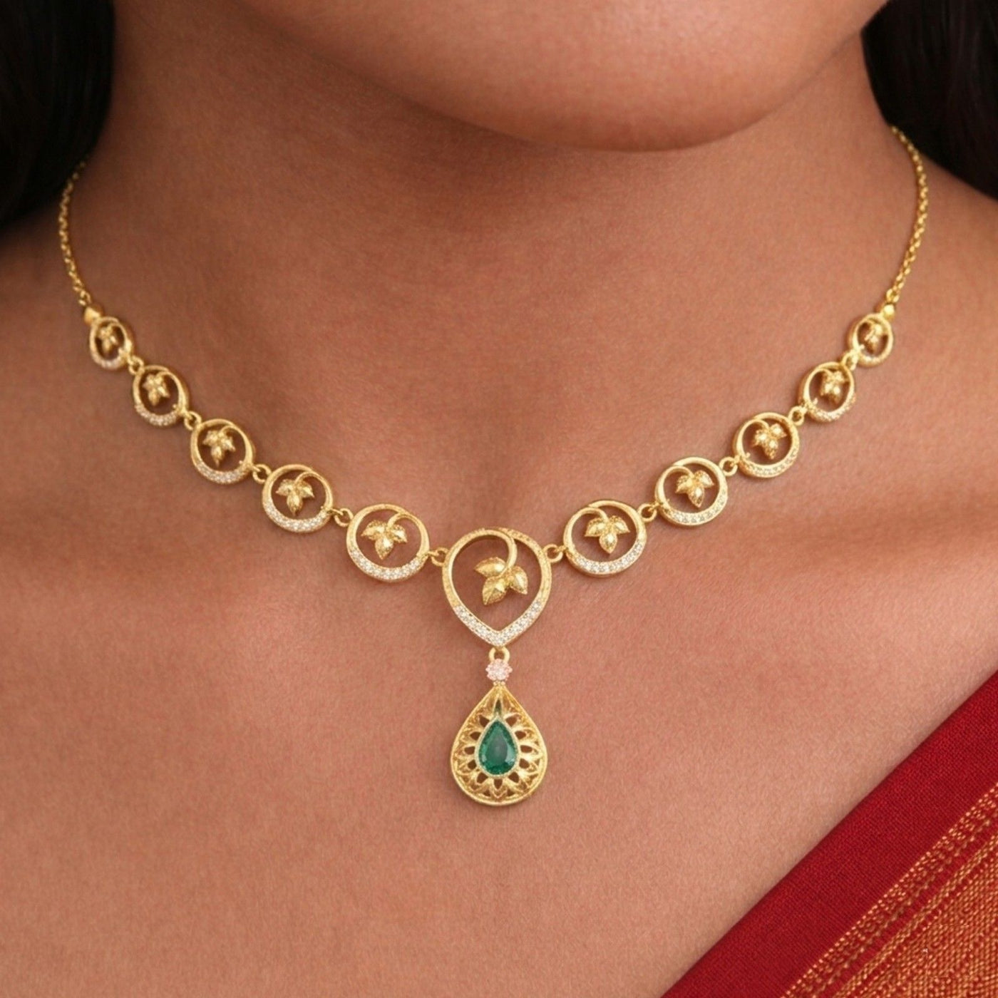 Gold and diamond necklace with a green gemstone on a person wearing a red saree.