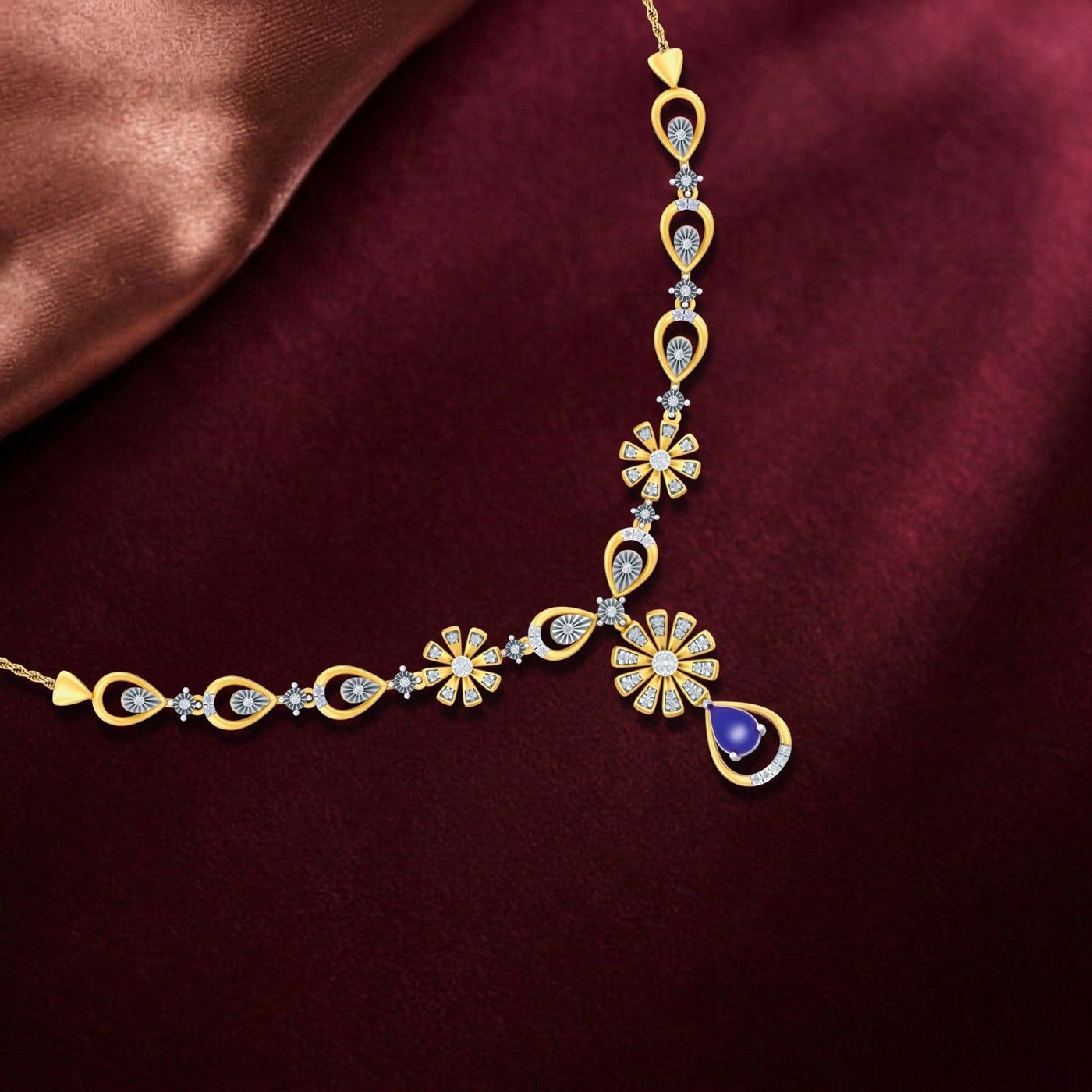 Gold necklace with floral designs and a blue gemstone on a maroon fabric background.