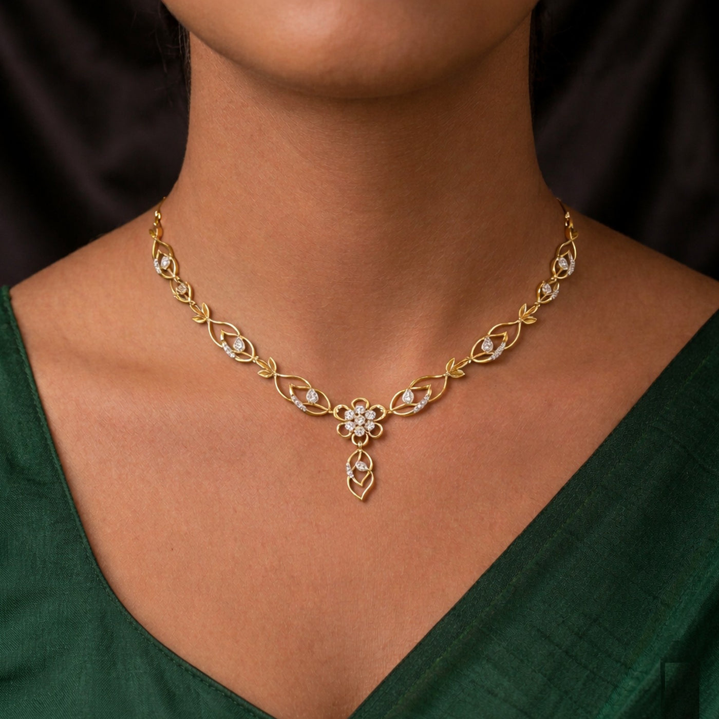 Gold necklace with floral design worn by a person in a green outfit
