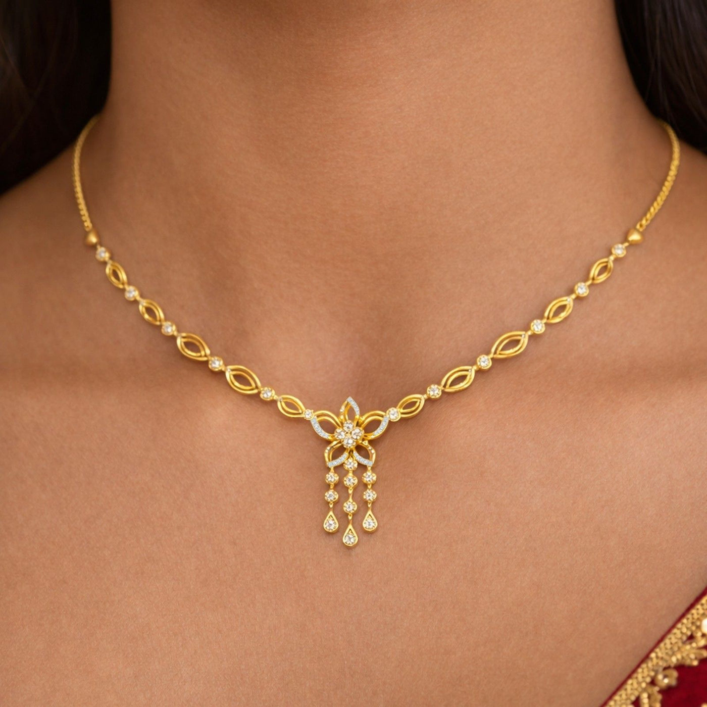 A close-up of a woman's wearing a gold necklace with a floral design and dangling teardrop charms.