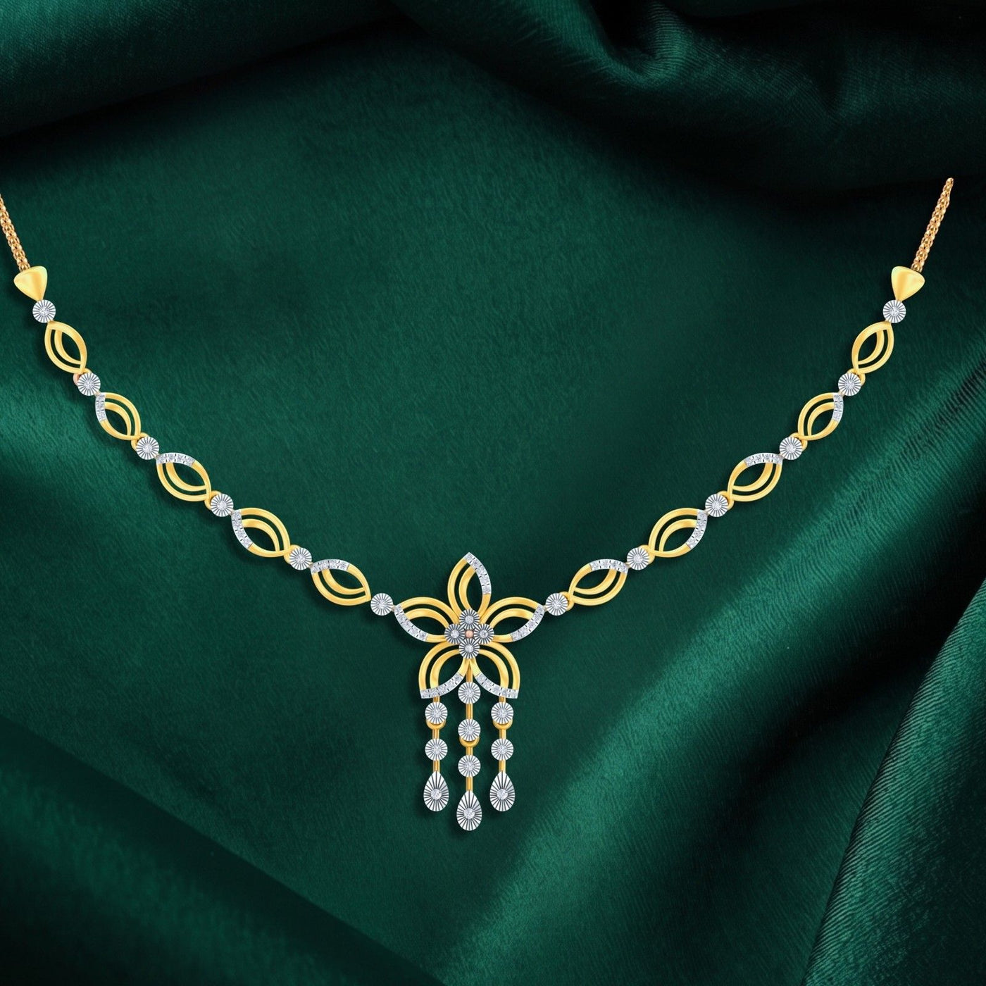 A gold and diamond necklace with a central floral motif and dangling teardrop charms, displayed on a draped dark green satin fabric.