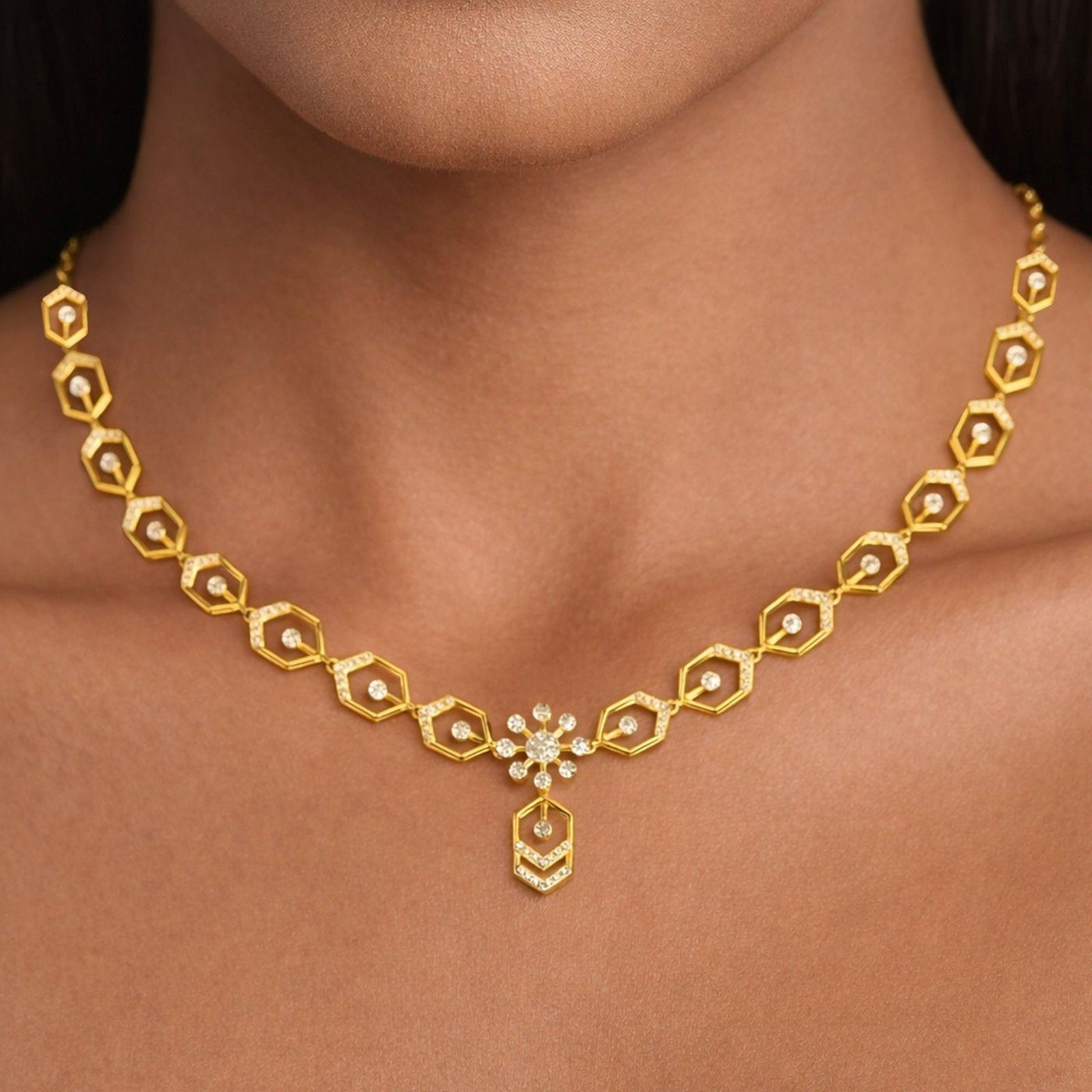 A gold necklace with a repeating hexagon pattern and a central floral pendant, shown worn on a model's neck.