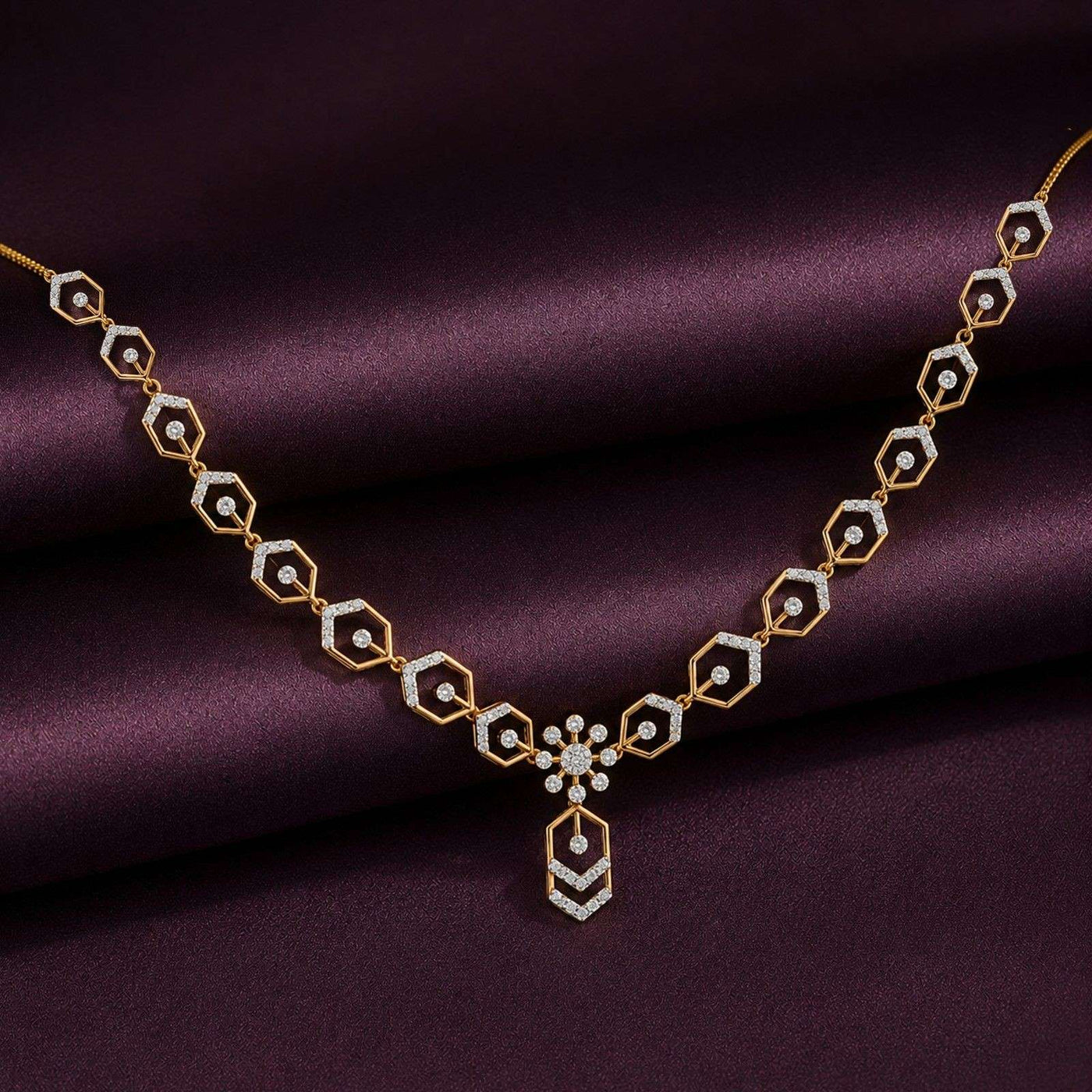 Gold and diamond necklace with a central floral starburst motif, displayed on draped dark purple satin fabric.