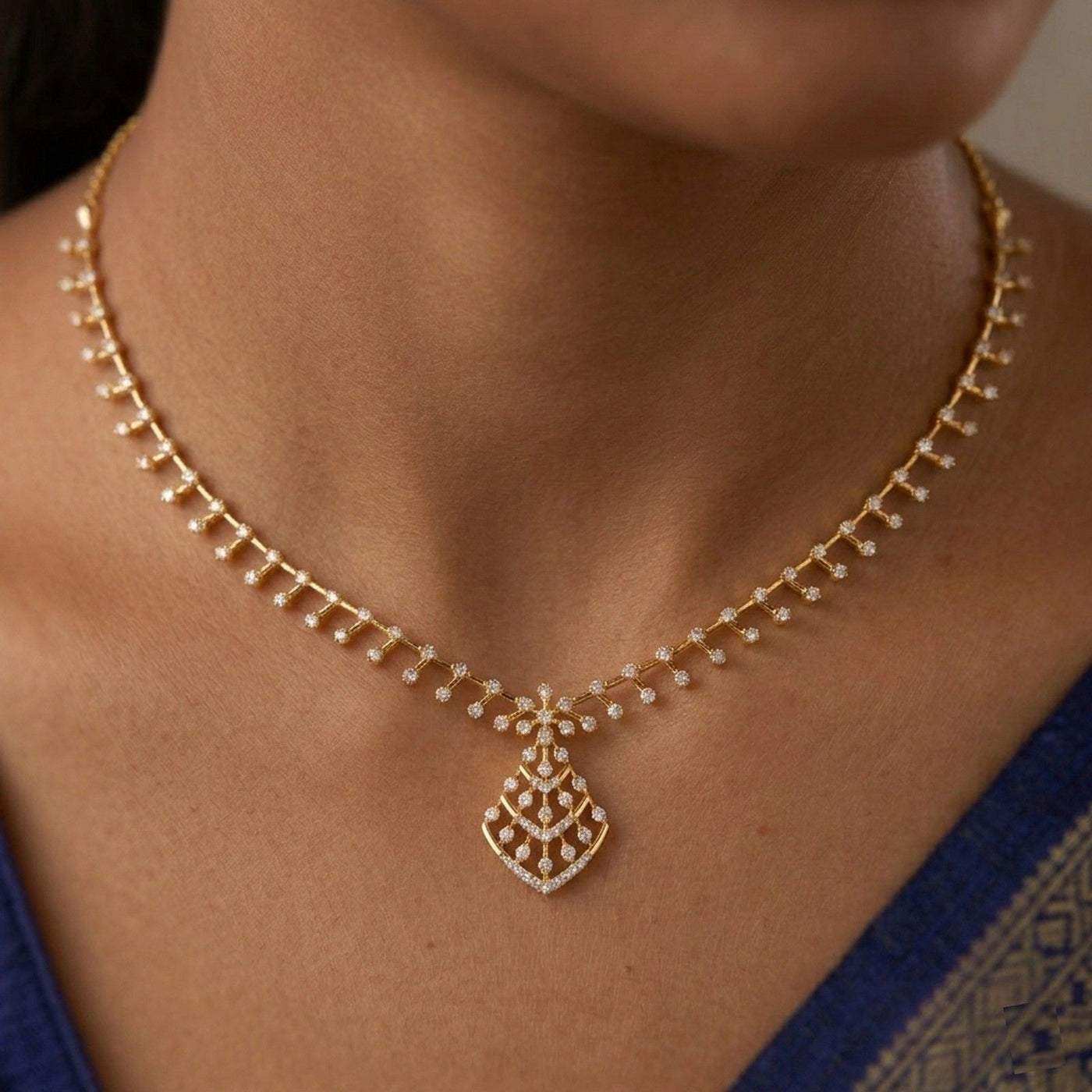 Gold necklace with a diamond on a person wearing a blue saree.