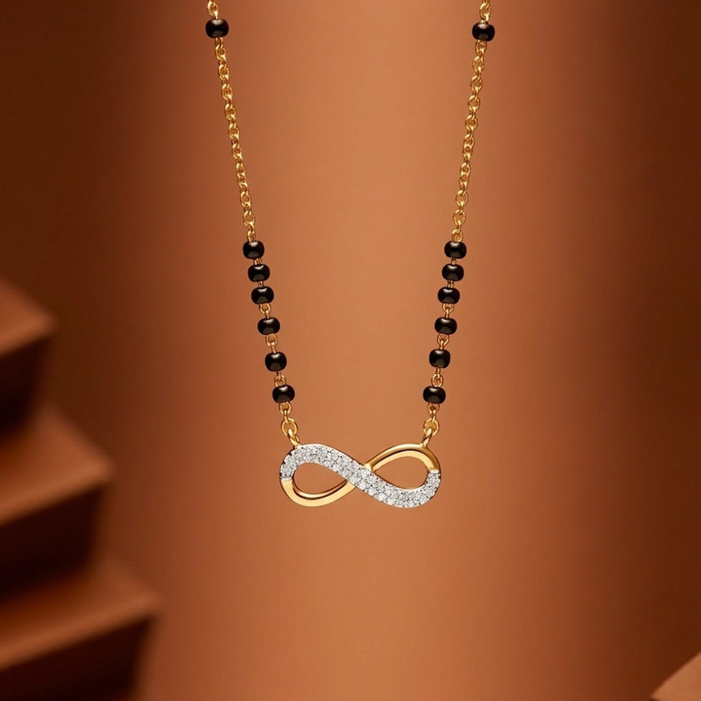 Gold diamond with black beads and a diamond-encrusted infinity symbol pendant on a brown background