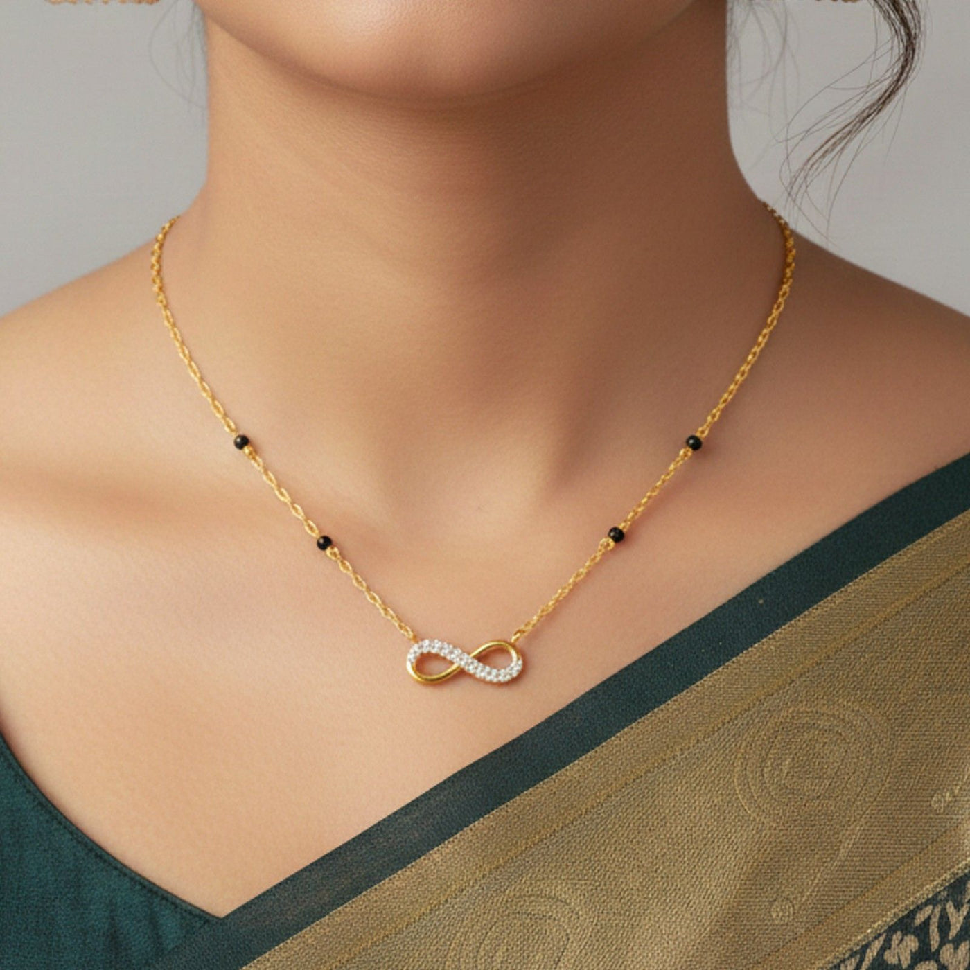 Gold pendat with a diamond infinity pendant worn by a model in a green saree.