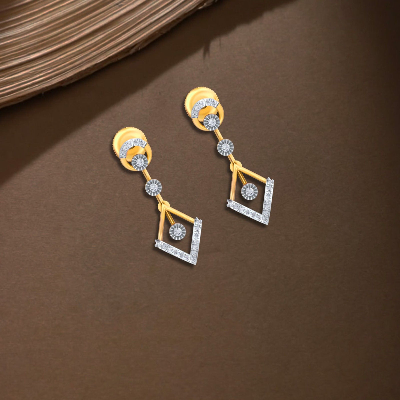 Pair of gold and diamond dangler earrings on a brown background.