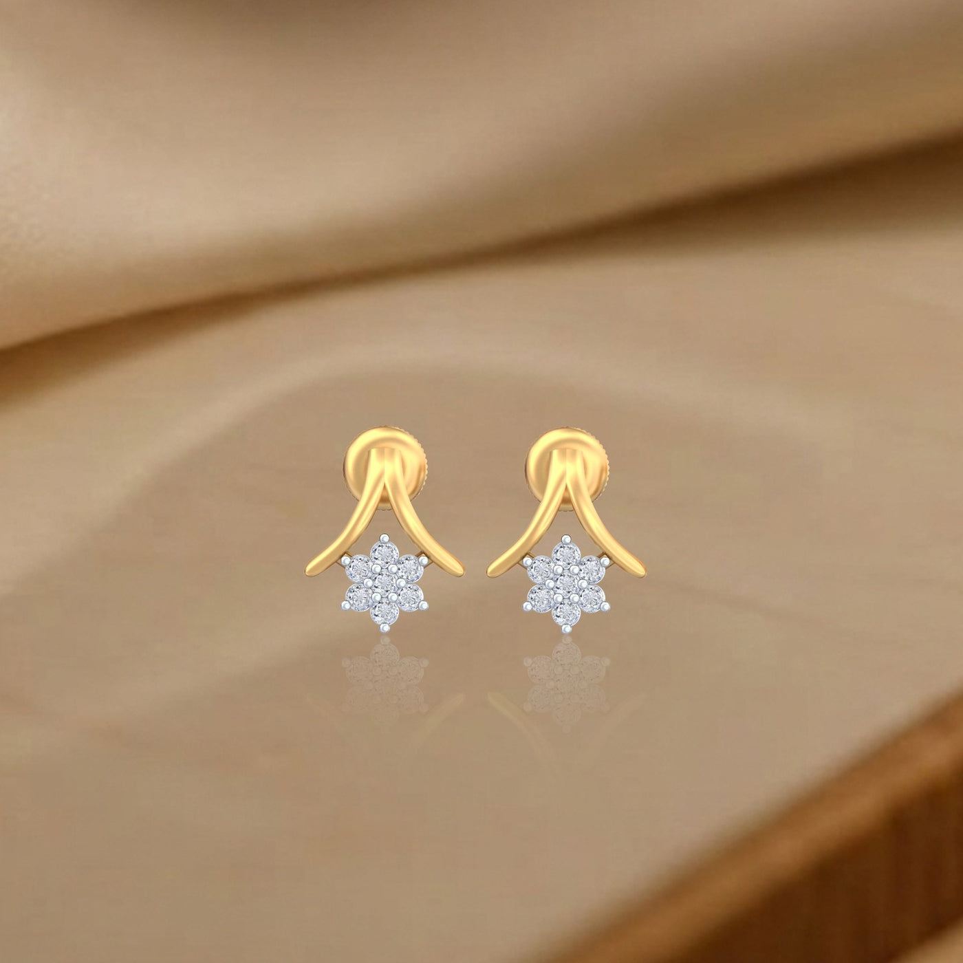 Gold and diamond stud earrings with floral design on a beige fabric background