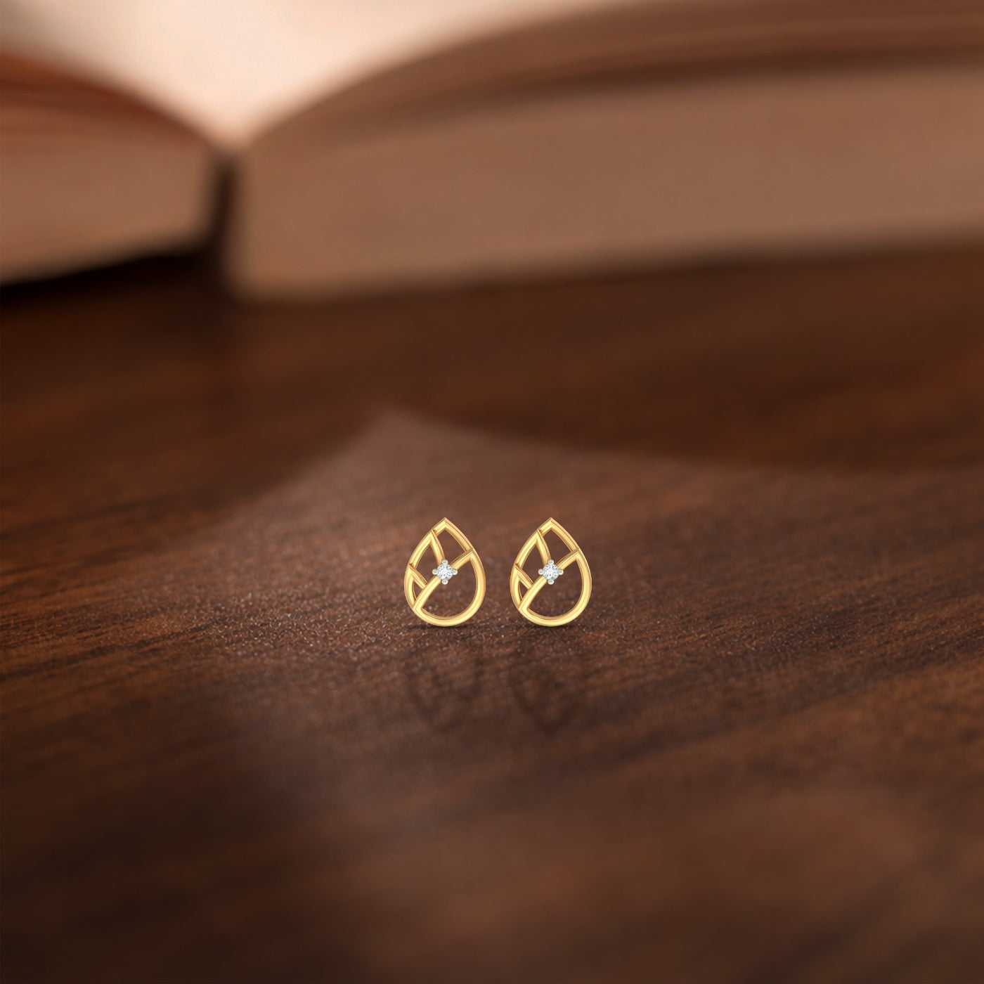 Gold and diamond teardrop-shaped stud earrings on a wooden surface