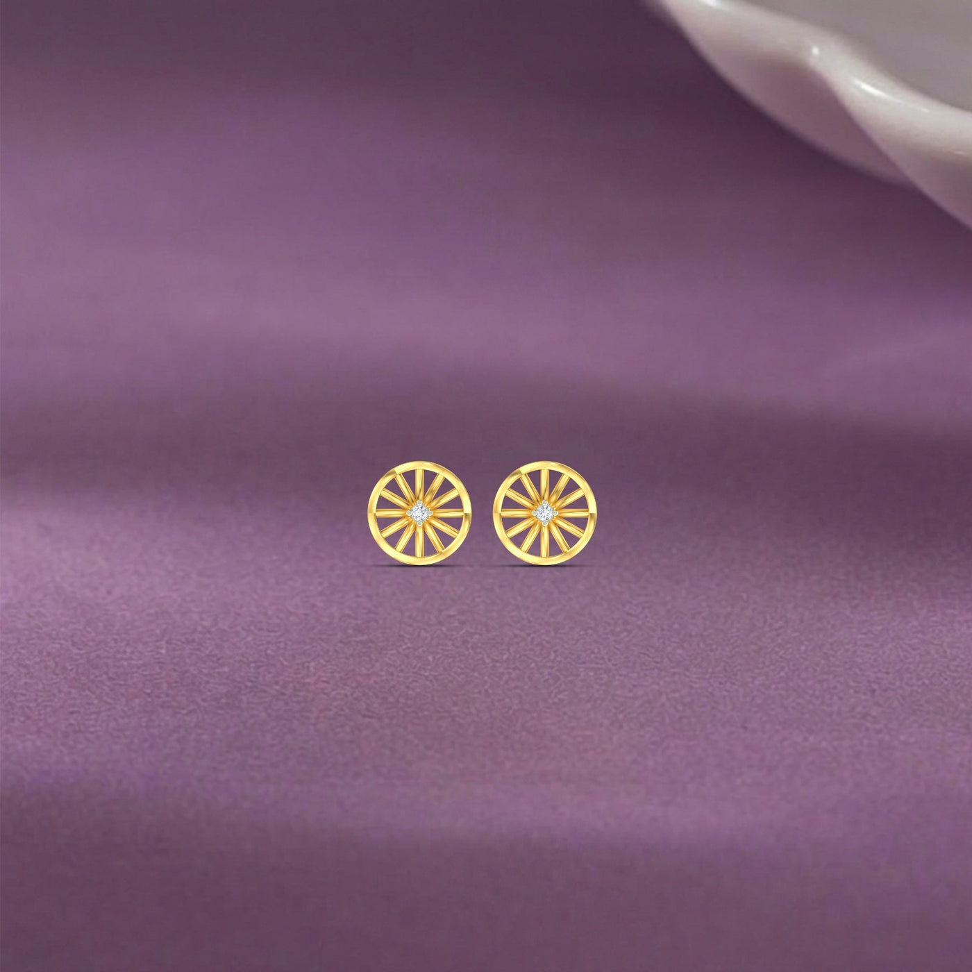 Gold and diamond stud earrings on a purple fabric background