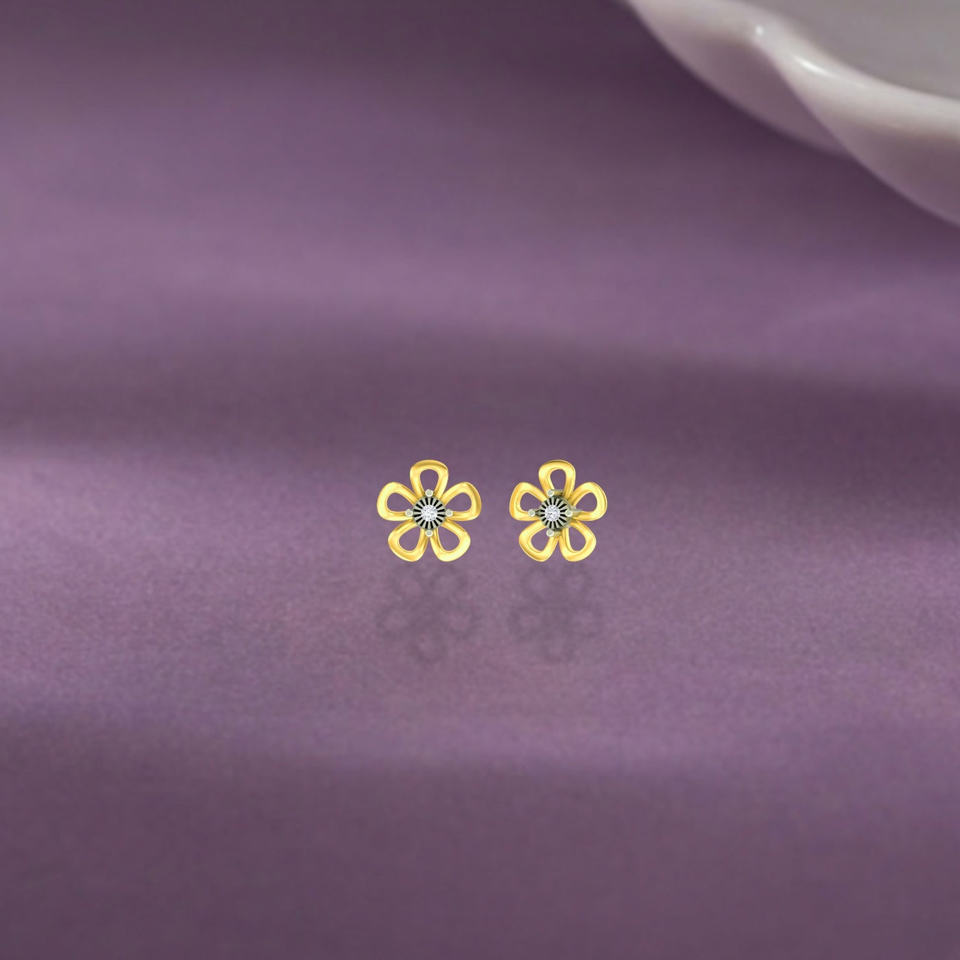 Yellow gold and diamond floral stud earrings on a purple fabric. background