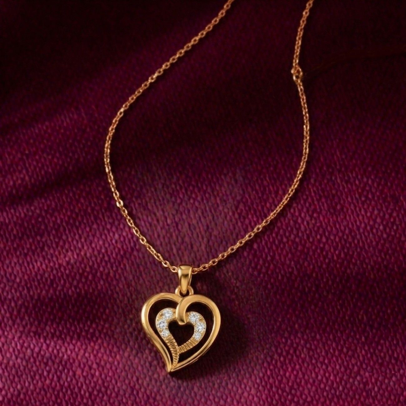 Gold heart-shaped pendant necklace on a maroon fabric background
