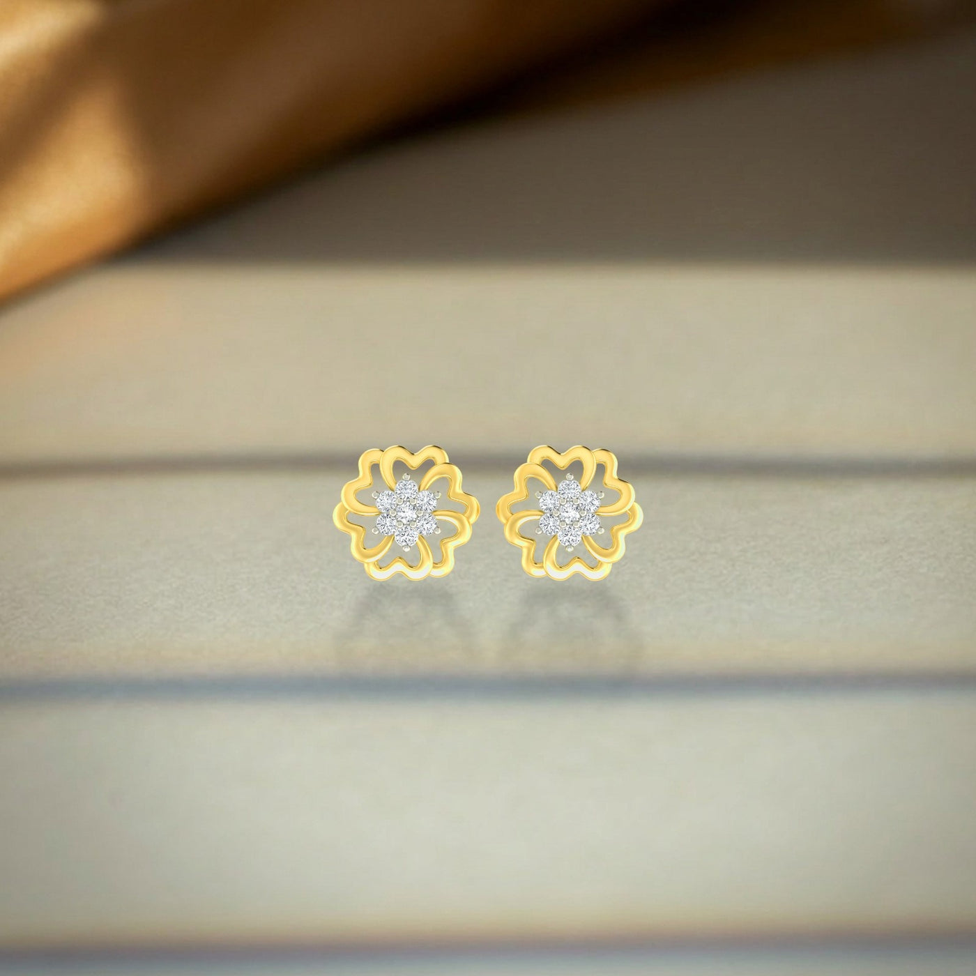 Gold and diamond floral stud earrings  on a beige fabric background