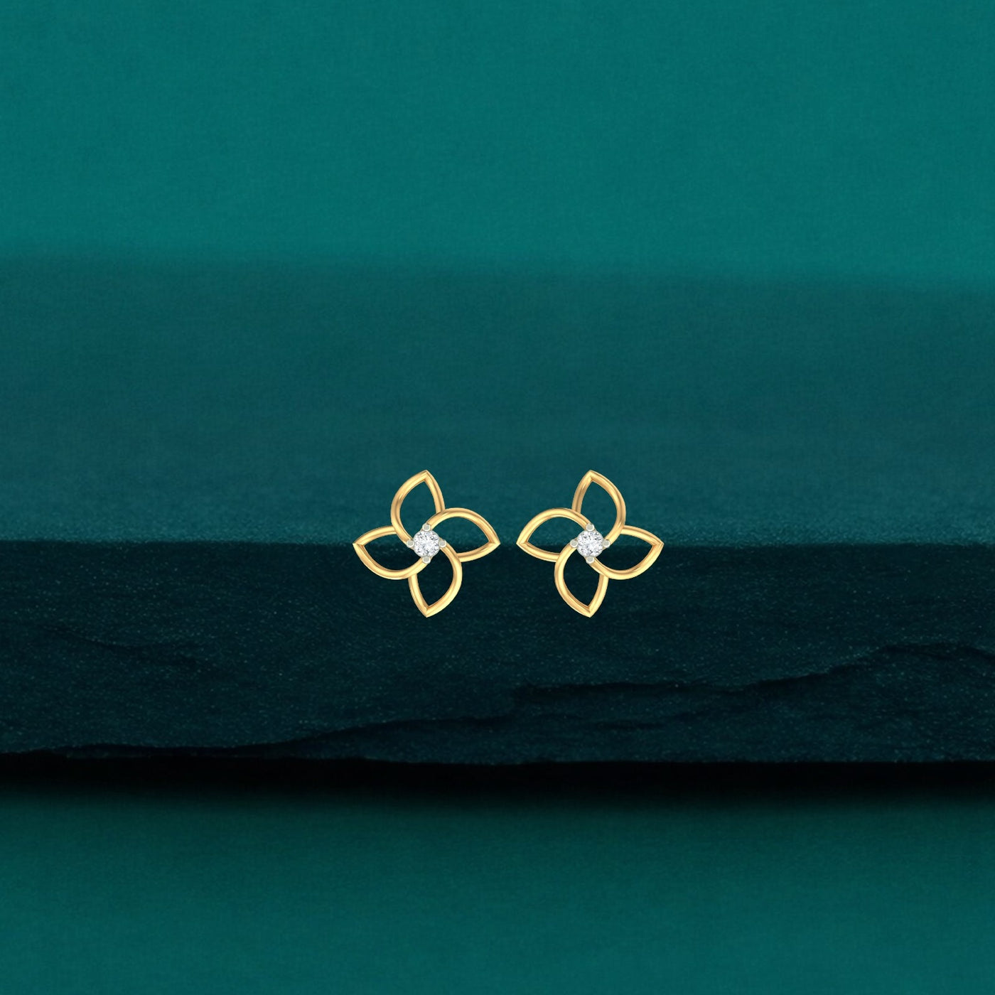 Gold and diamond floral stud earrings on a teal fabric background