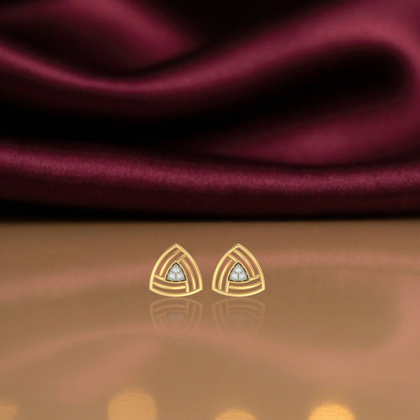 Gold and diamond stud earrings on a reflective surface.