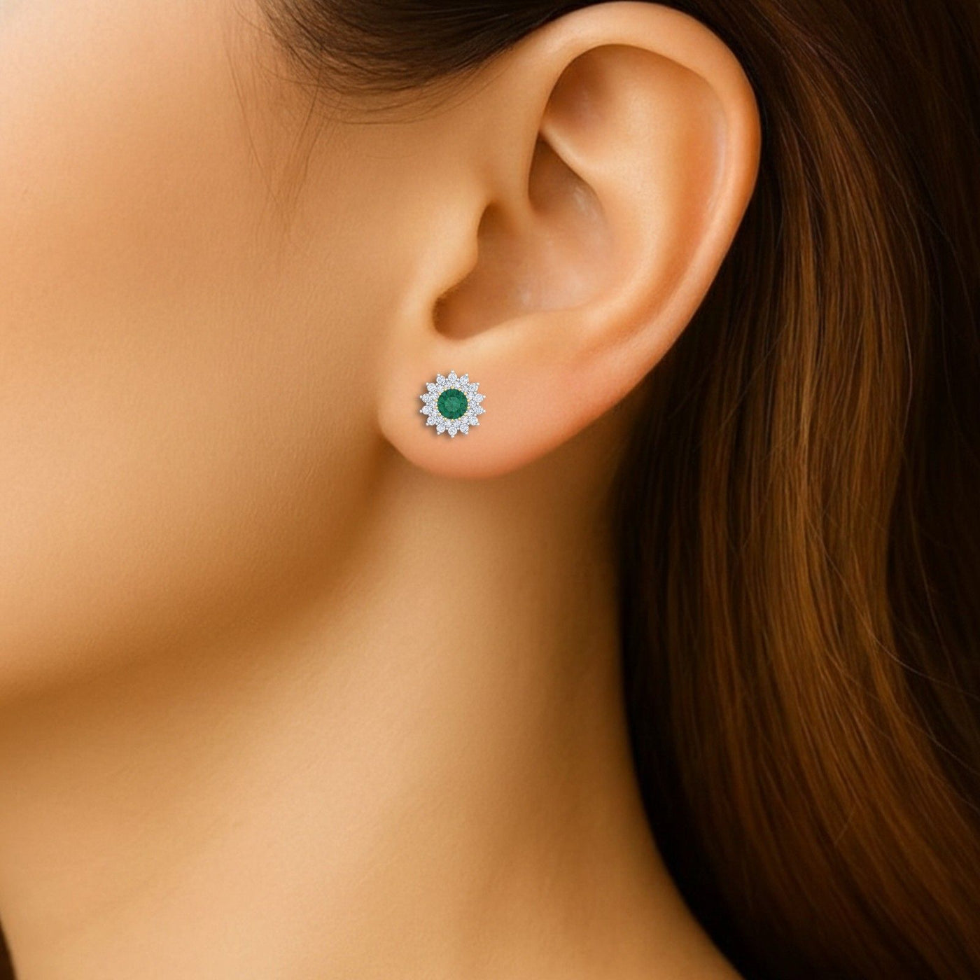 Close-up shot of a pair of gold and diamond stud earrings with emerald gemstone.