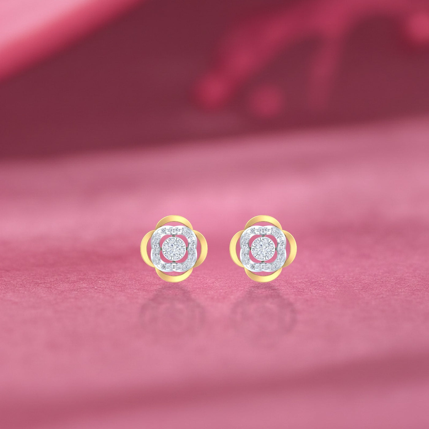Gold and diamond floral-design stud earrings on a pink surface background.