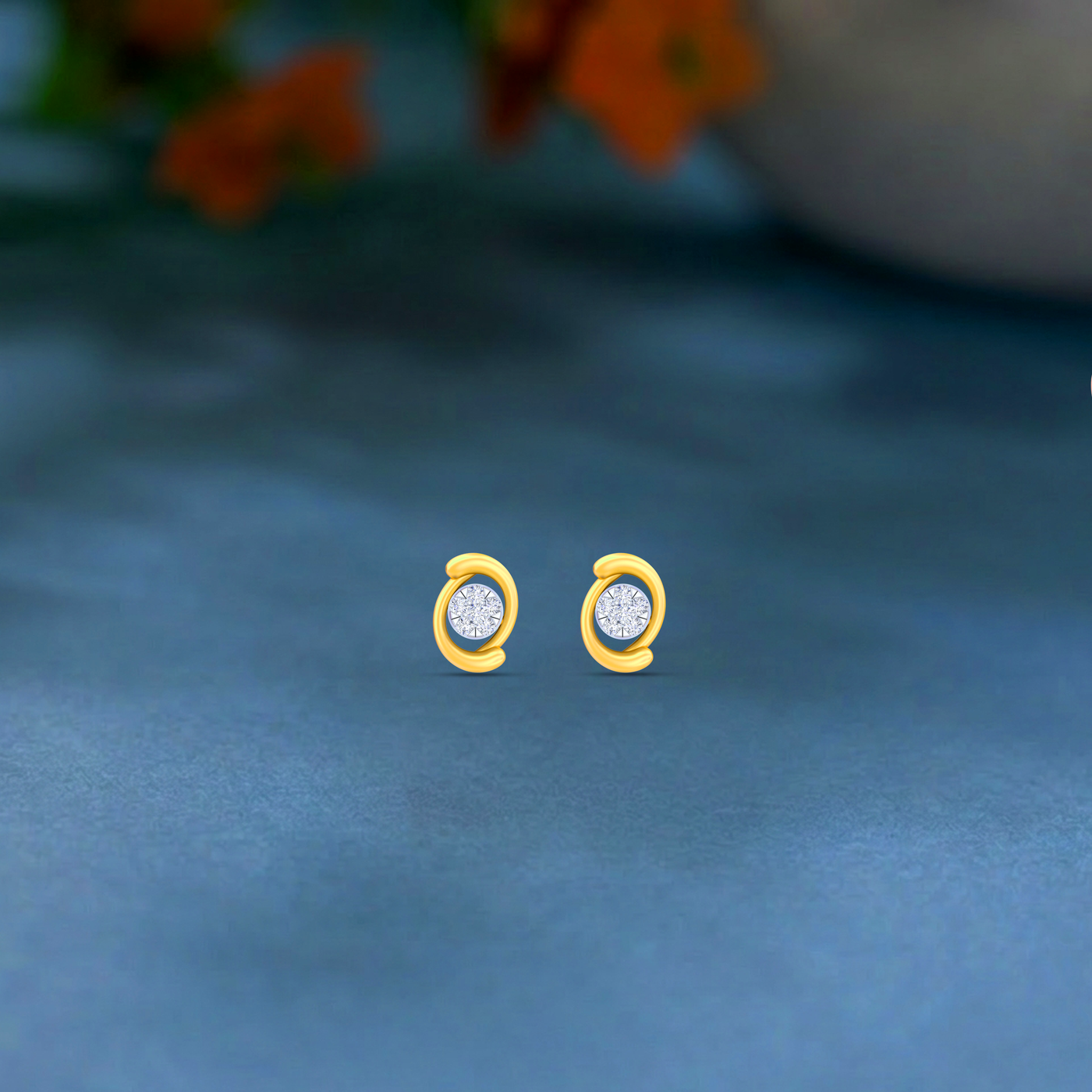 Gold and diamond stud earrings with circular design on a blue surface