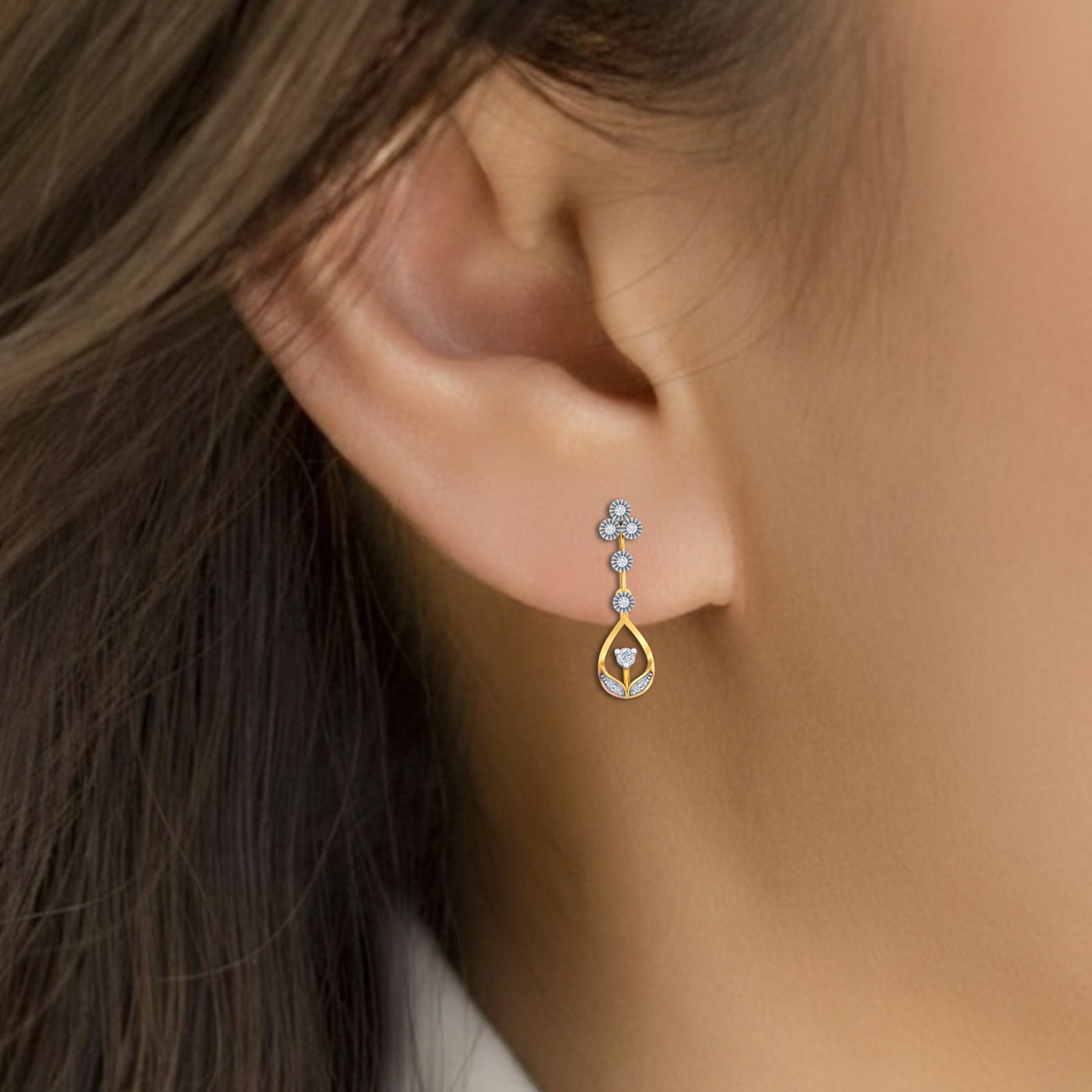 Close-up of an ear wearing a gold and diamond earring with a blurred background.
