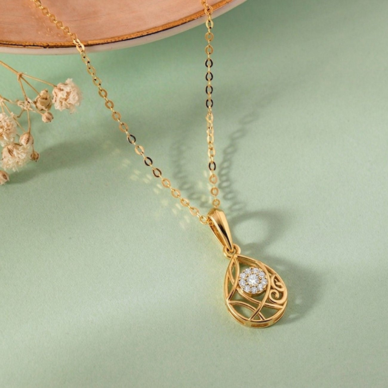 Gold necklace with a teardrop-shaped pendant on a light green background