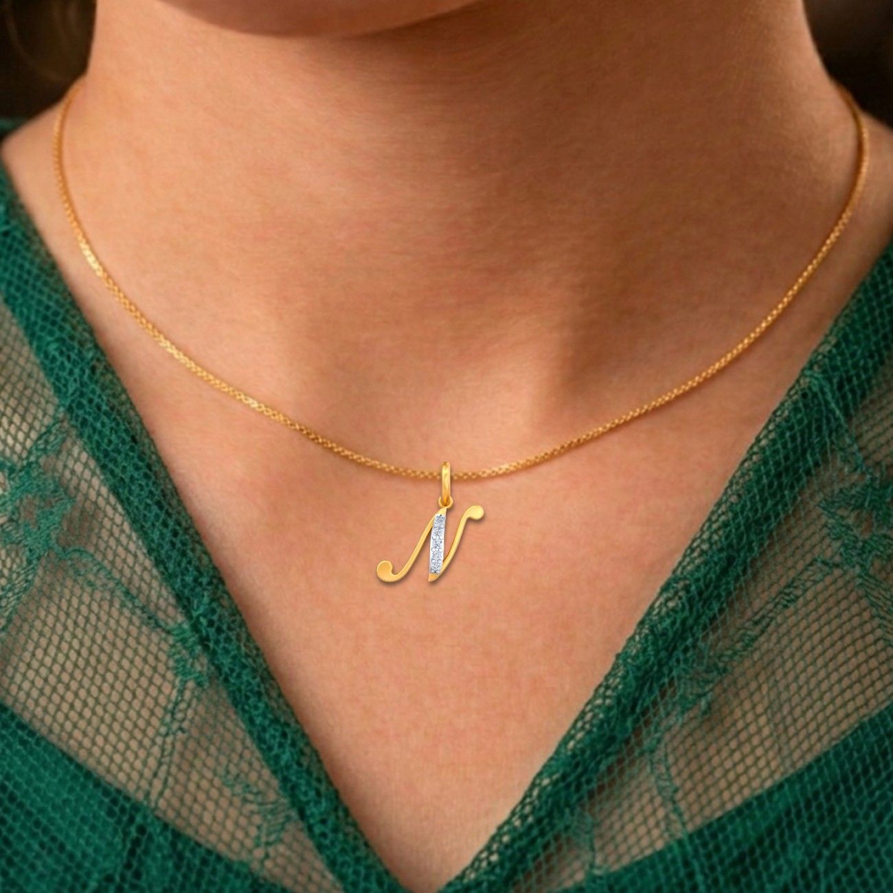 Gold necklace with a 'N' pendant worn by a person in a green lace garment.